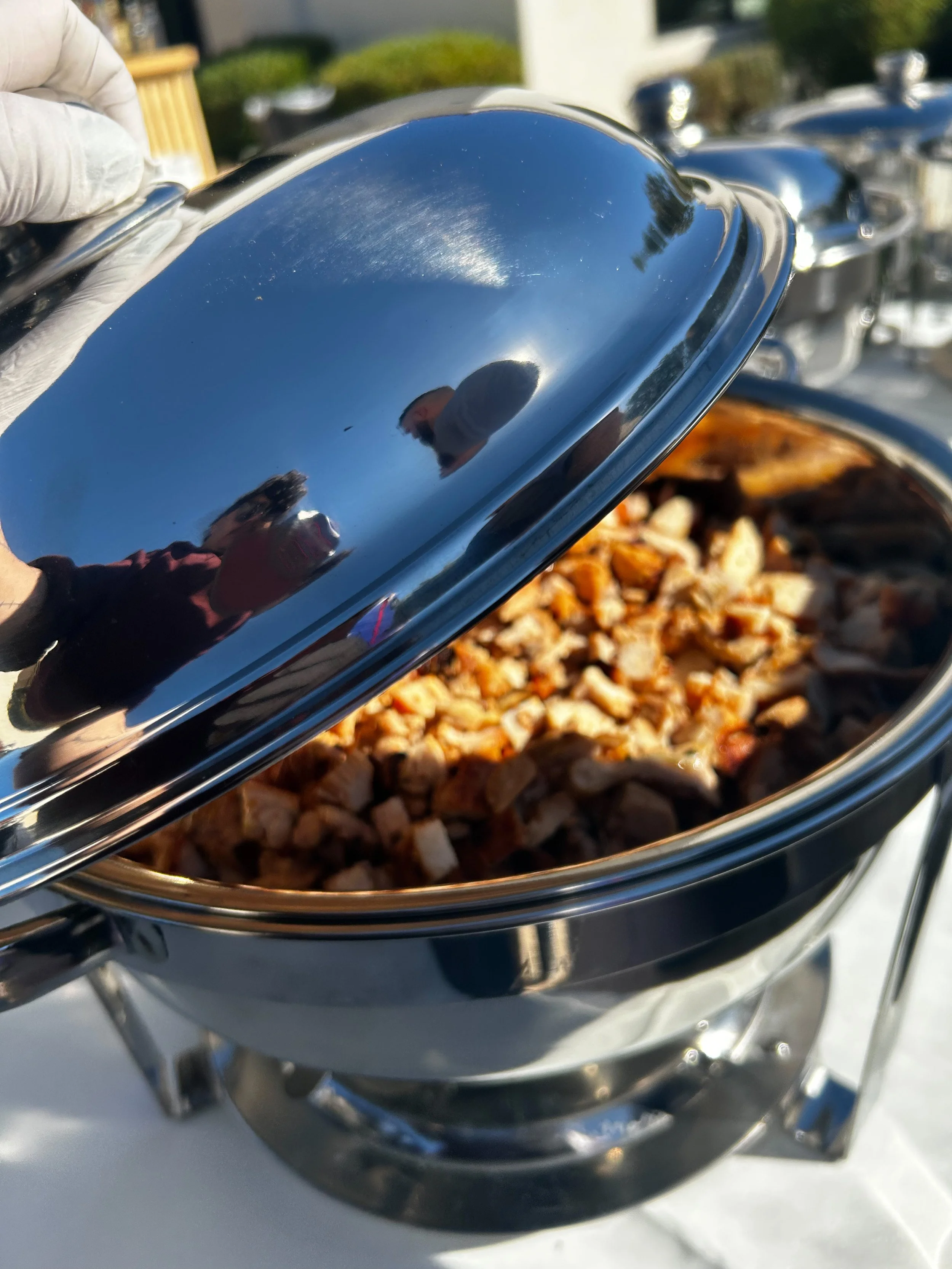 A chafing dish with a partially opened lid, revealing cooked diced chicken in the dish.