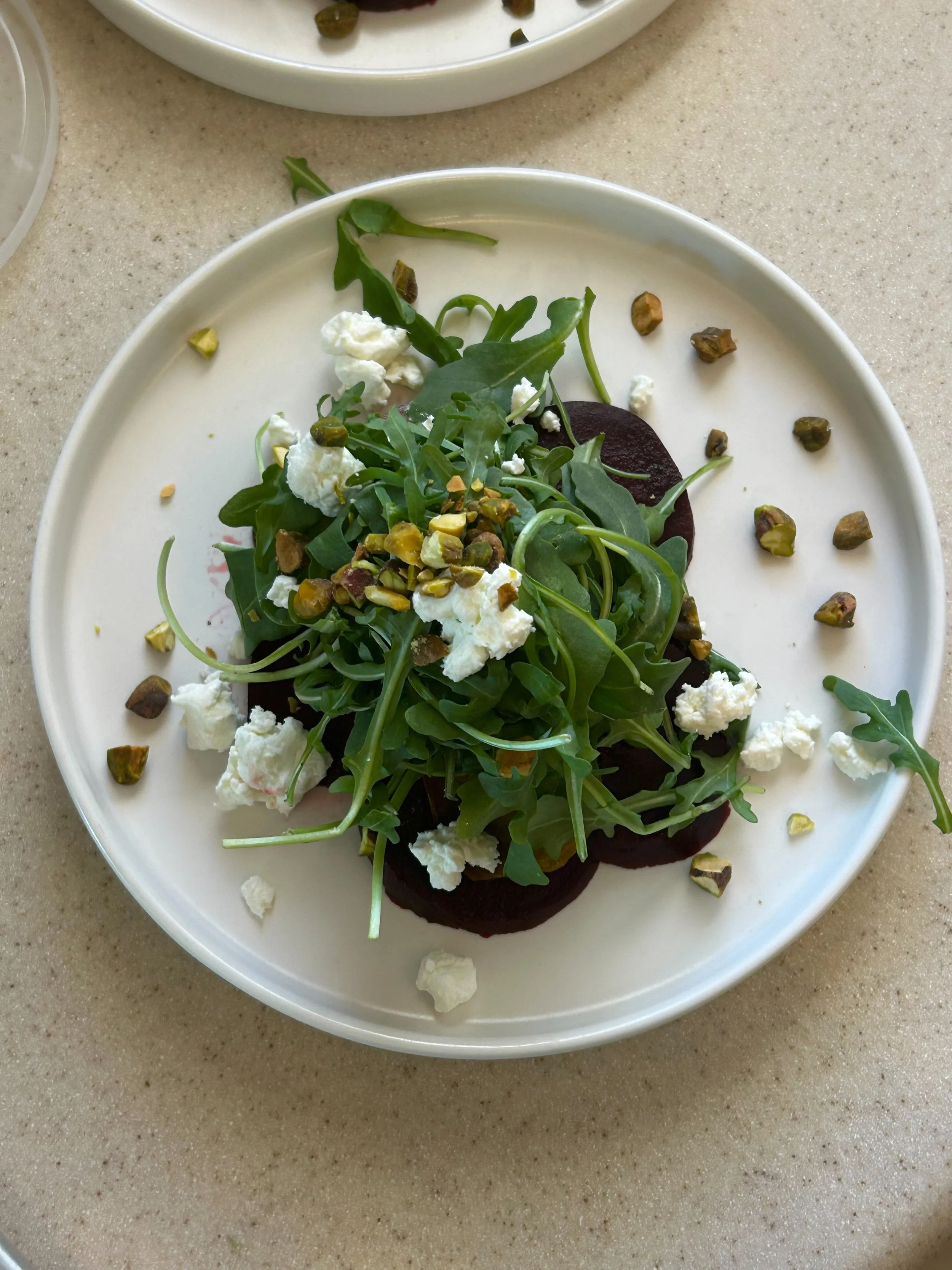 Salad with arugula, beets, goat cheese, and chopped pistachios on a white plate.