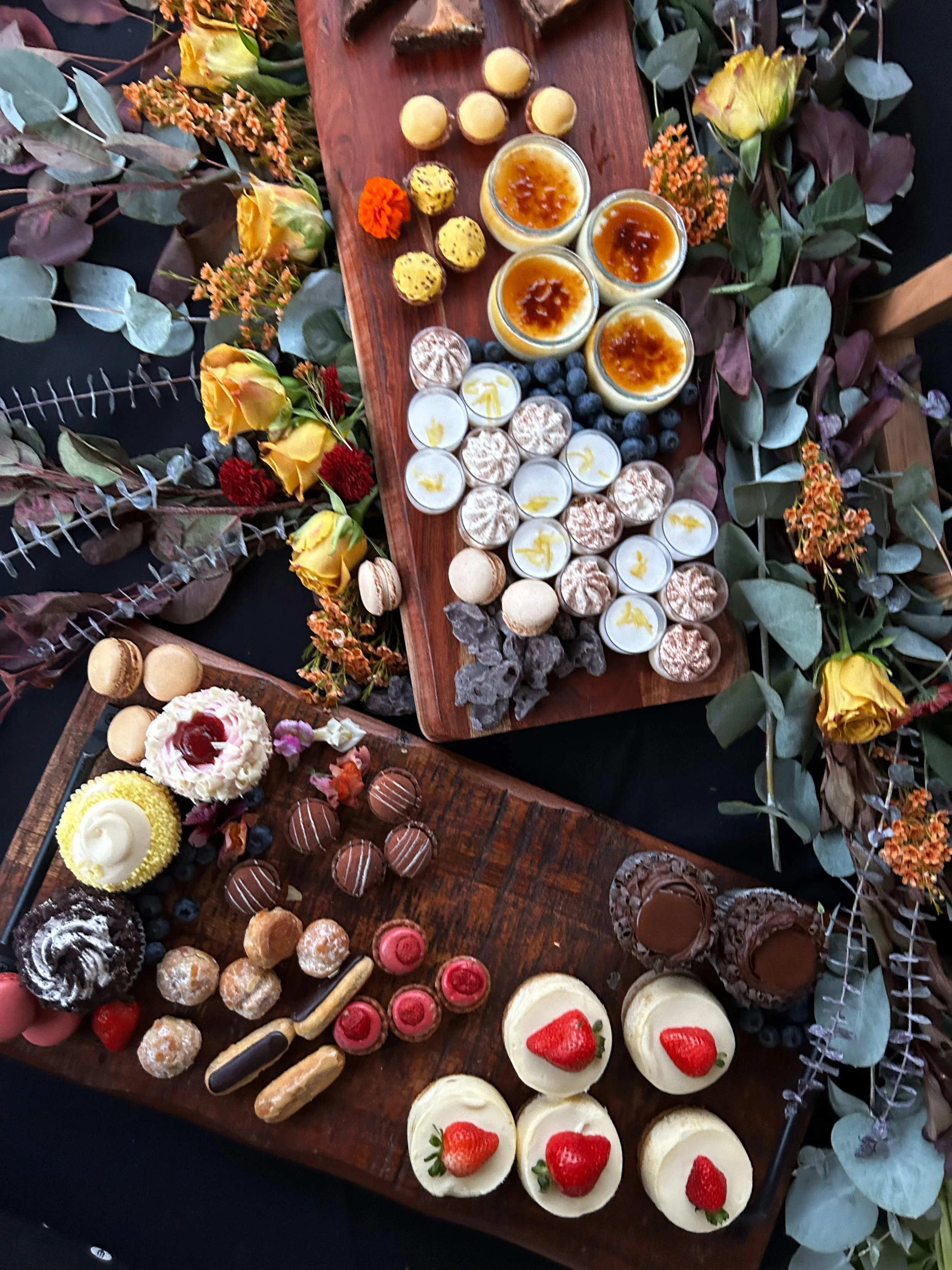 Assorted desserts on wooden boards surrounded by decorative flowers and leaves.