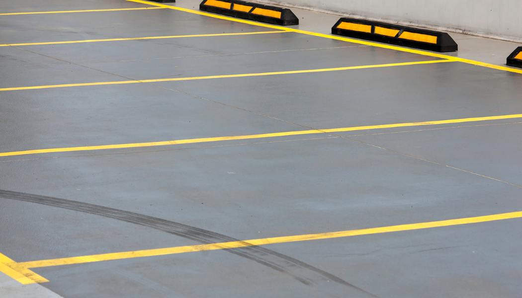 Empty parking lot with yellow parking space lines and wheel stops at the end of each space.