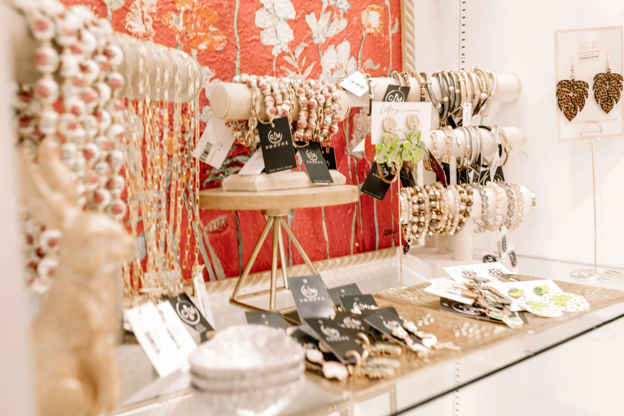 Display of jewelry including bracelets, earrings, and necklaces on a table and stand in a boutique with decorative background.