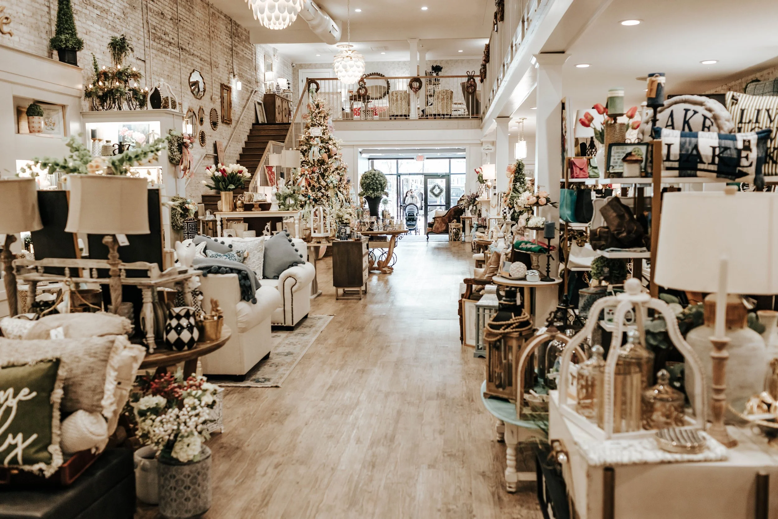 Interior of a cozy boutique decorated for Christmas with a Christmas tree, flowers, pillows, and various home decor items displayed on shelves and tables.