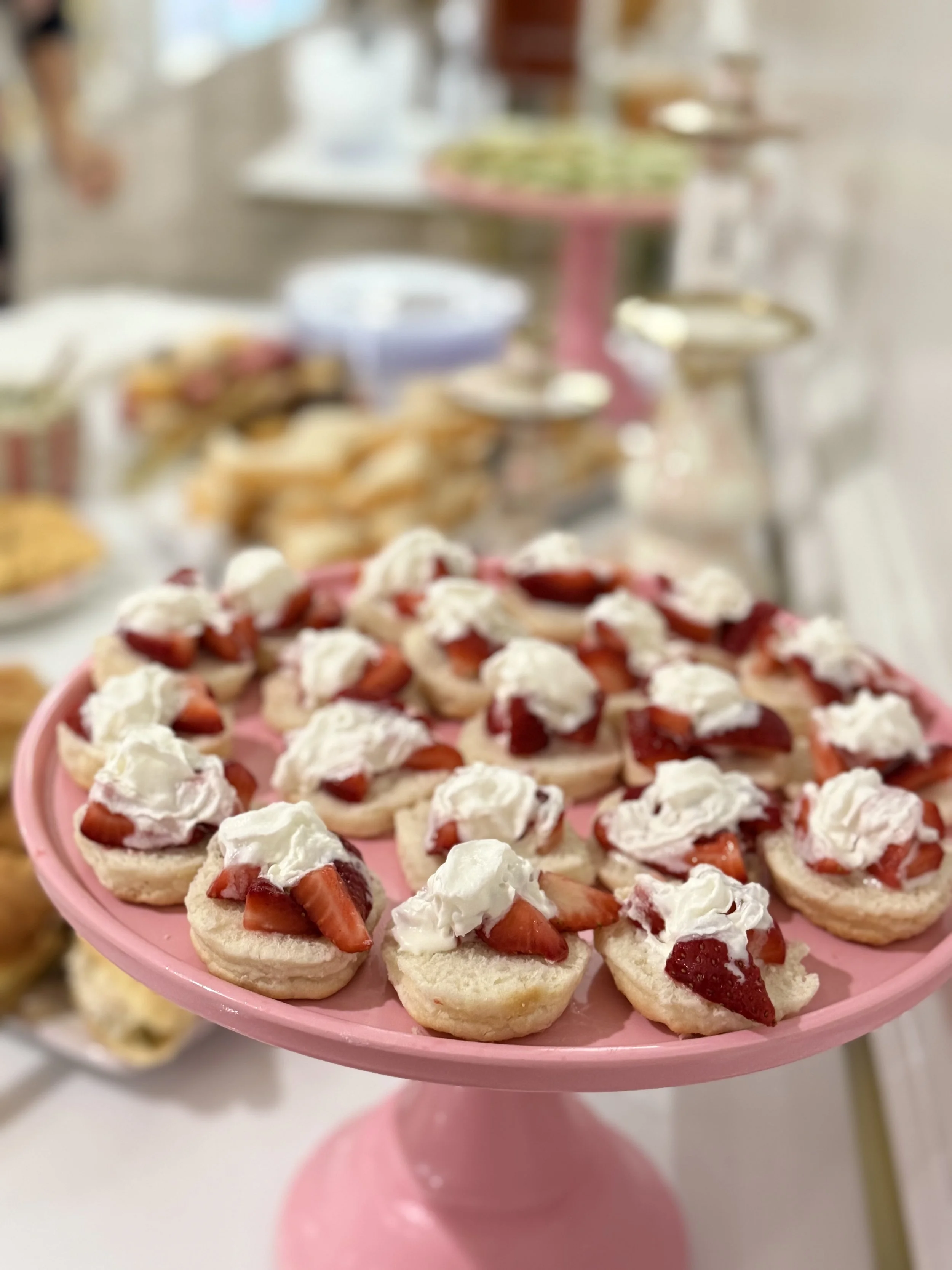 Mini strawberry shortcake desserts with whipped cream on a pink cake stand.