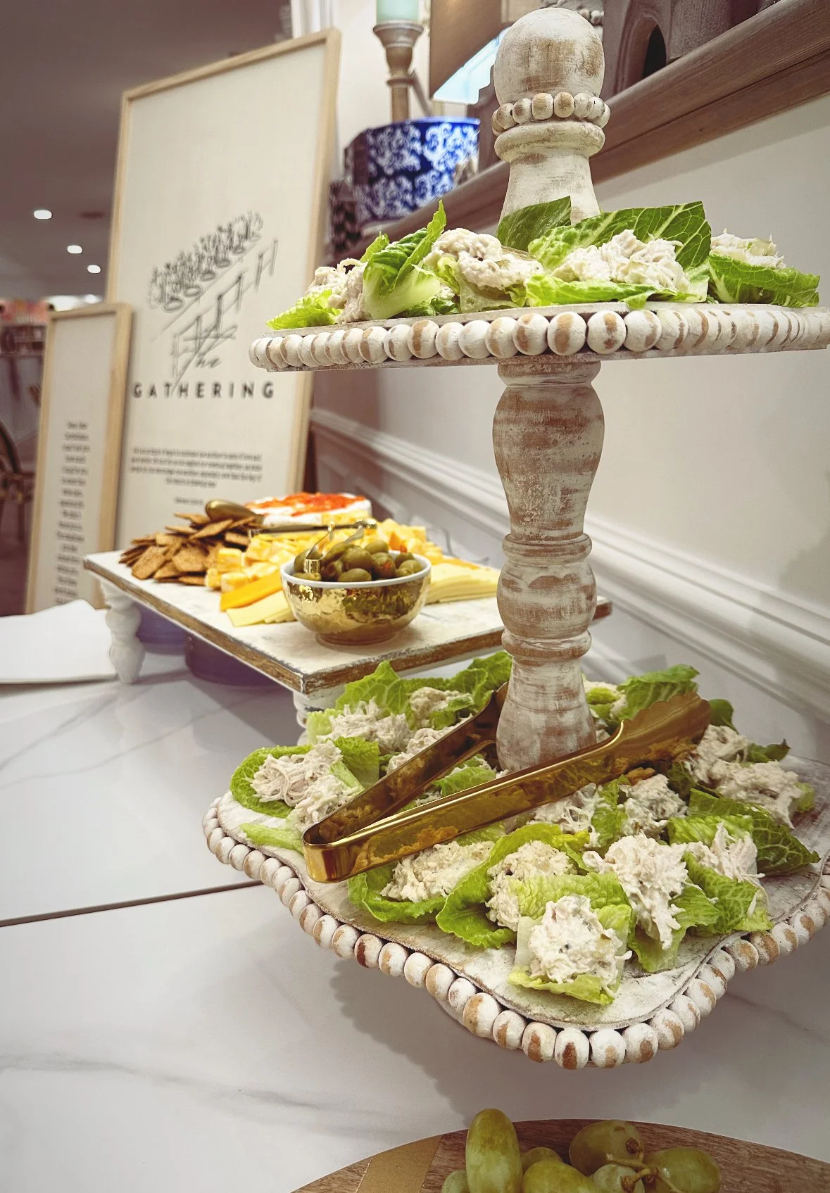 Two-tiered appetizer tray with lettuce wraps and chicken salad, on a white table with a grazing sign in the background.