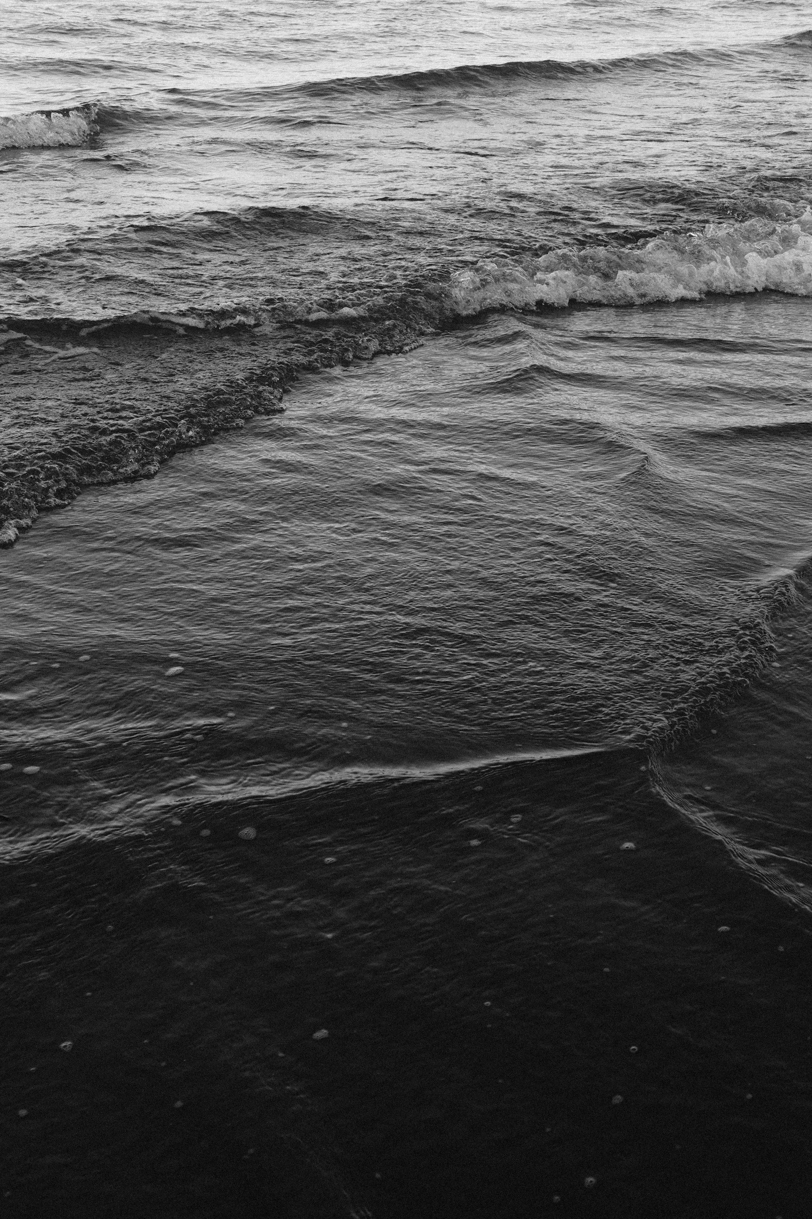 Black and white photo of ocean waves gently lapping at the shore.