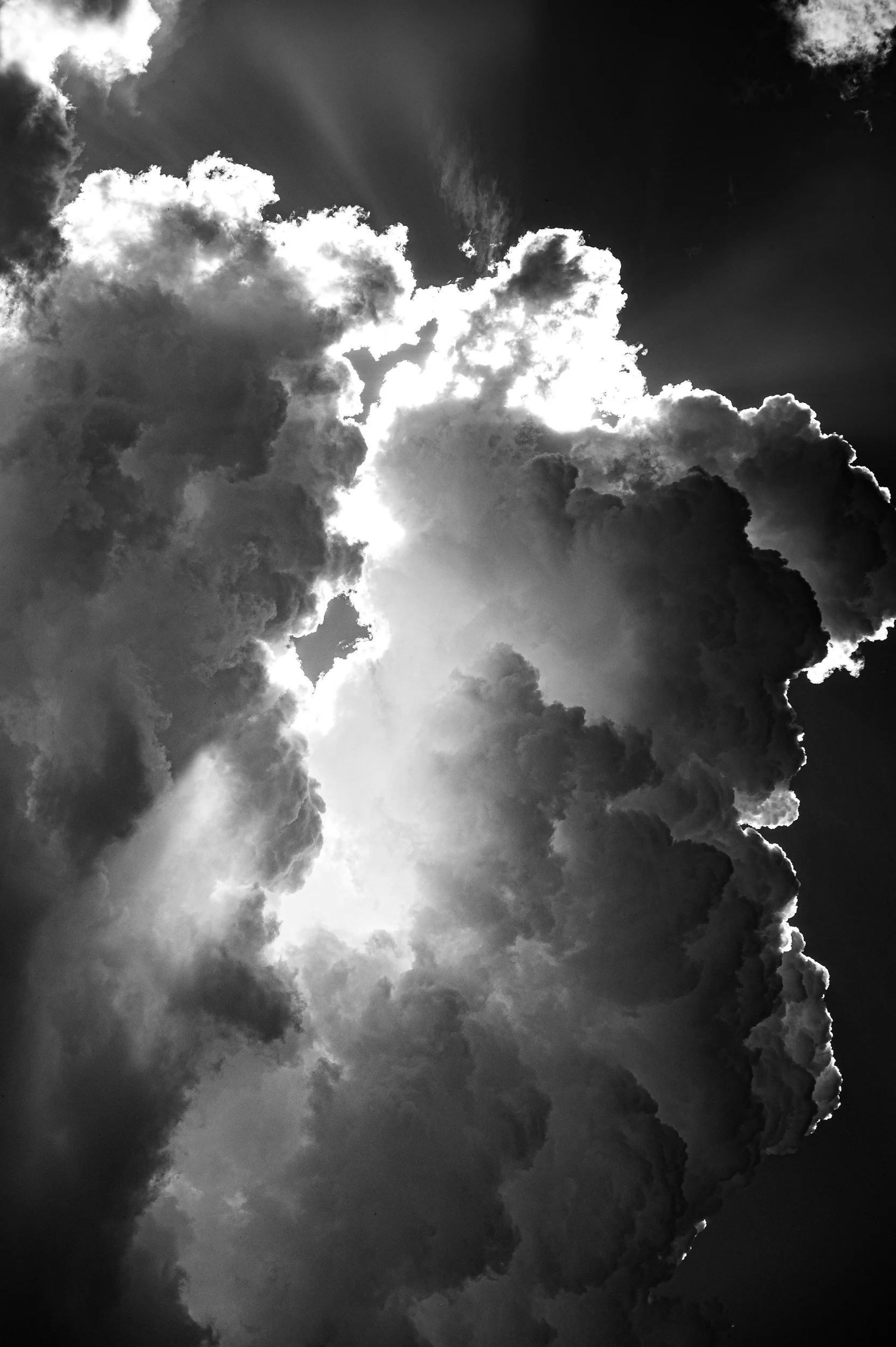 Black and white photograph of large, dramatic clouds with sunlight breaking through.