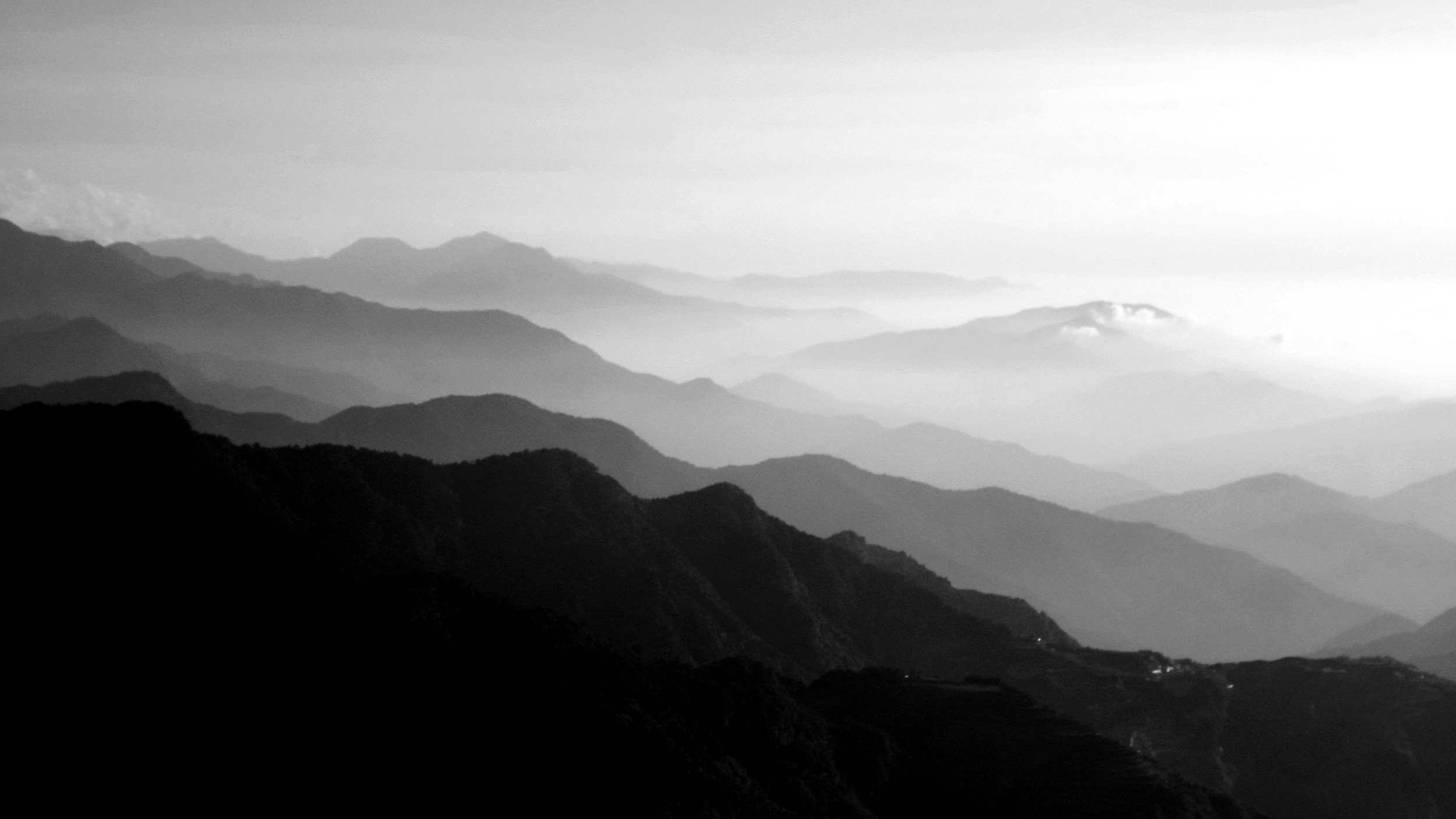 Black and white photograph of layers of mountains fading into the distance under a cloudy sky.