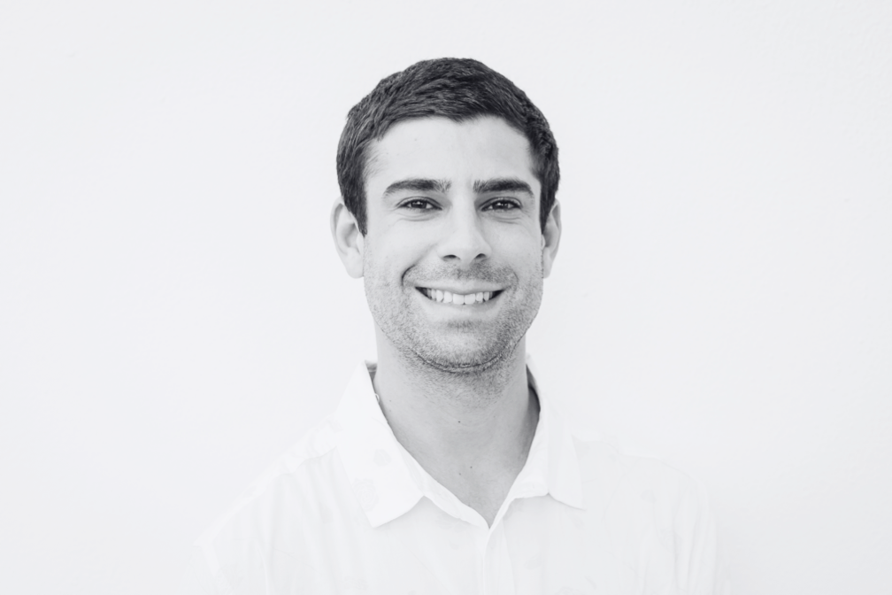 Portrait of a smiling young man with short dark hair, wearing a white collared shirt, against a plain white background.