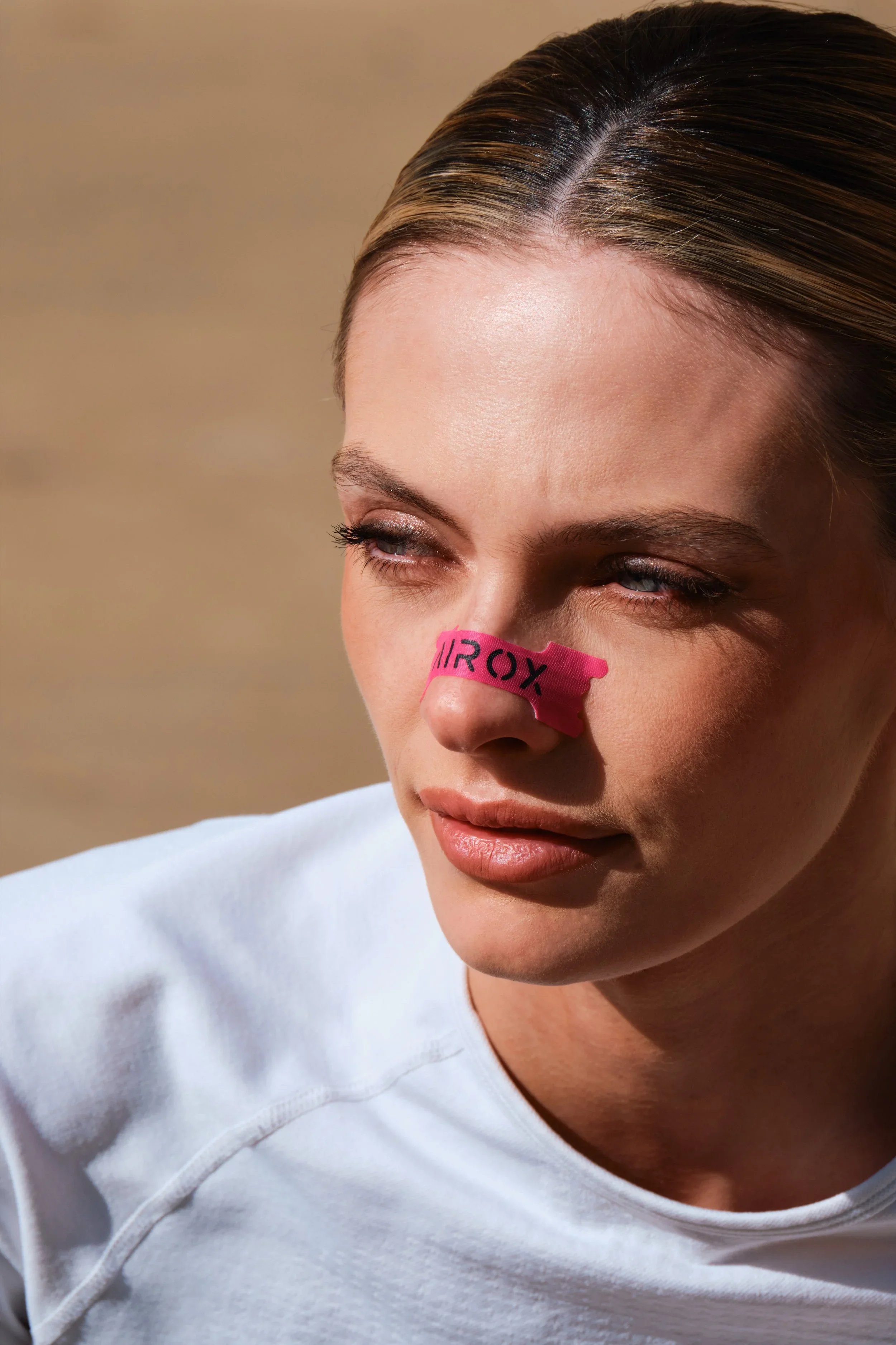 A woman with blonde hair, wearing a white top, has a pink sticky note with the word 'TROXY' on her nose.