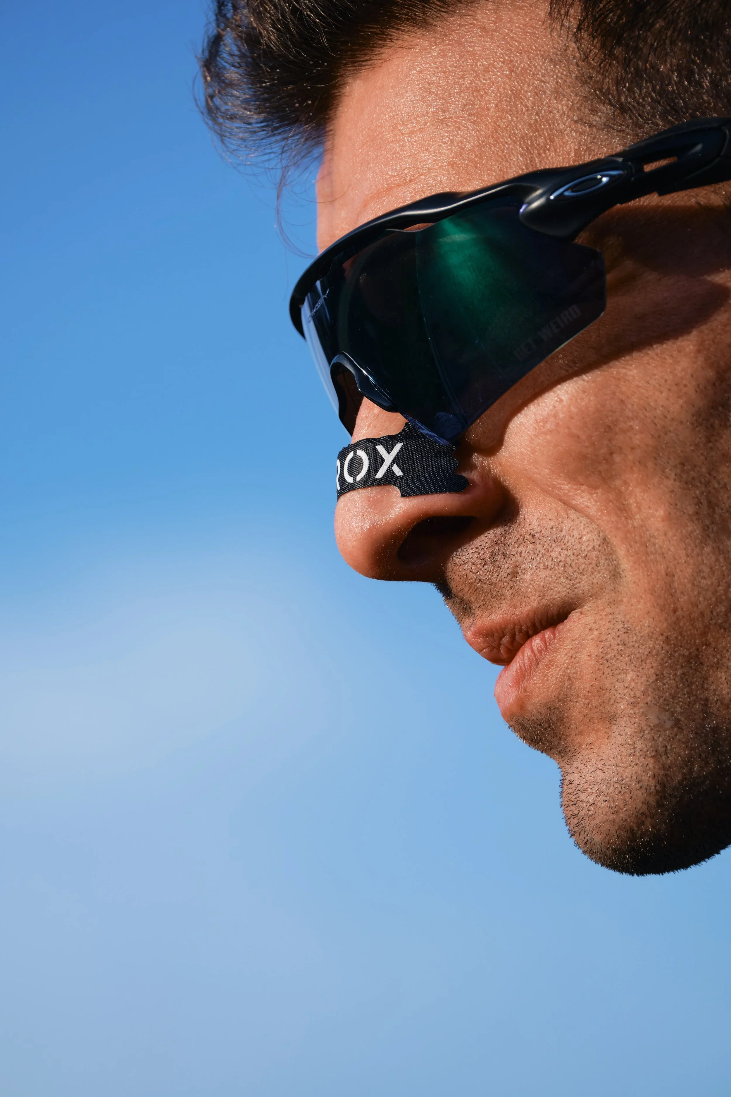Close-up of a man wearing sports sunglasses against a clear blue sky.