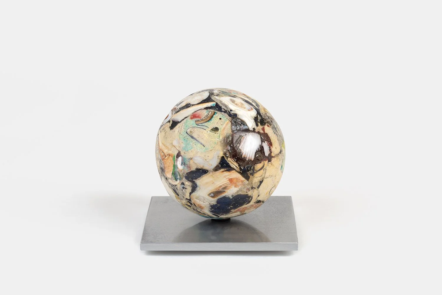 Yasue Maetake Orb Materia—Silken, 2026. Spherical form with soft beige, black, and white mineral surfaces containing a prominent ridged shell fragment, resting on a square aluminum base.