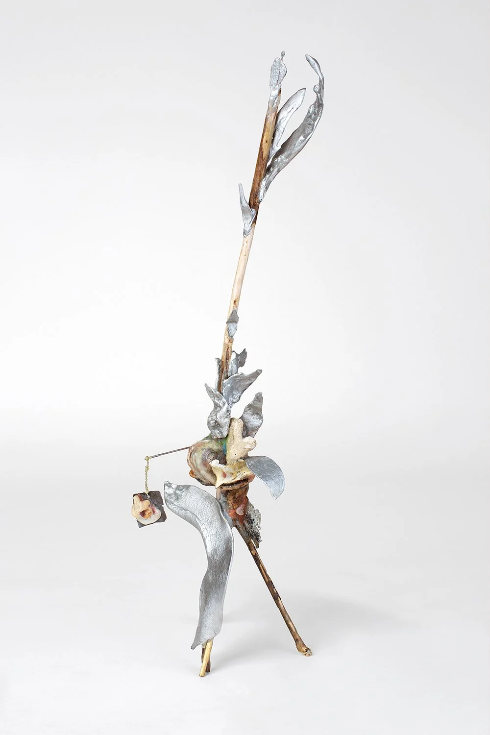 Abstract sculpture made of natural and metallic materials, resembling a walking stick with added elements, set against a plain white background.