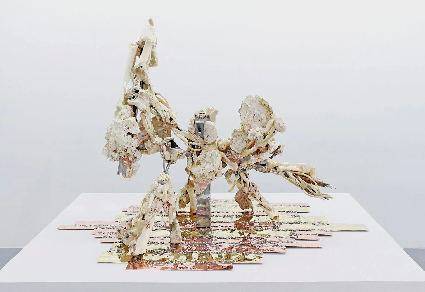 Yasue Maetake’s sculpture Lineal Fetishism I, 2021. Horizontal hybrid assemblage of white bone and fossil forms combined with metal elements, resting on layered copper and brass plates against a white background.