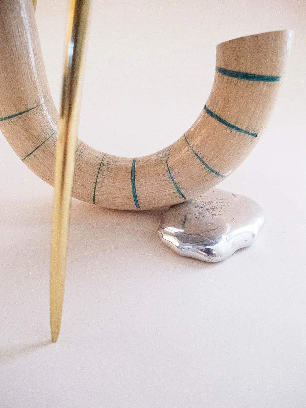 Close-up of a decorative object featuring a curved wooden element with blue lines, supported by a silver base, and a yellow vertical element in the foreground.