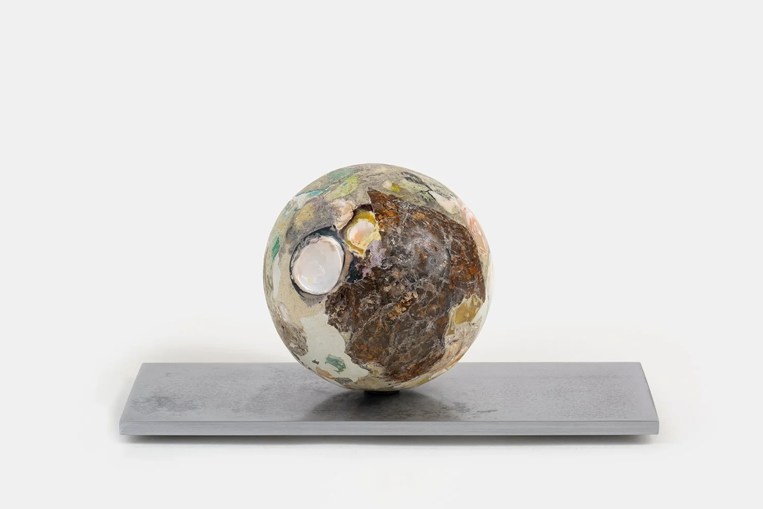 Yasue Maetake Orb Materia—Cocoon, 2026. Spherical form with soft beige mineral surface, a large dark organic textured area, and an open white shell cavity, resting on a rectangular aluminum base.