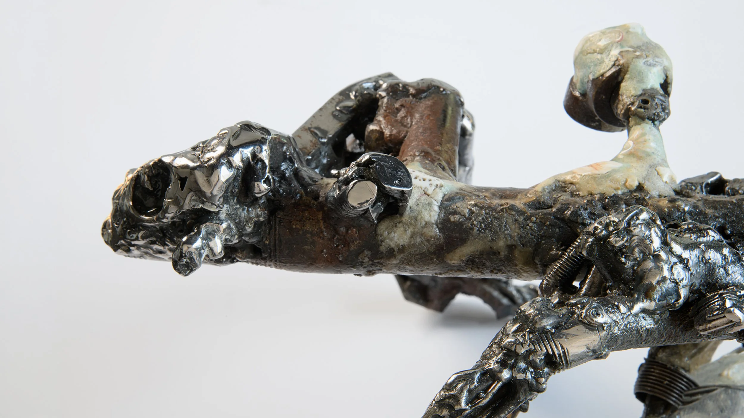 Yasue Maetake Mare Fecunditatis extreme close-up: dark twisted metallic form with beige accretions, holes, and eroded textures against white background