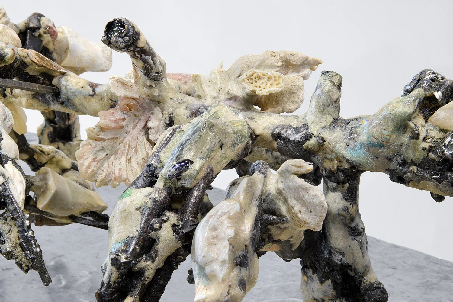 Yasue Maetake's sculpture Mare Fecunditatis – resurrection, 2025. Close-up detail of the hybrid surface featuring prominent shiny dark metallic elements with rough, craggy texture and embedded organic forms, surrounded by porous white structures and 