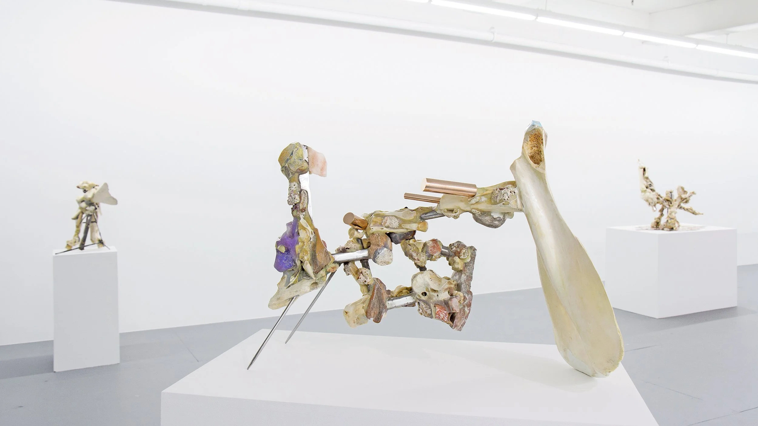  Yasue Maetake Transmutation gallery installation: non-representational sculpture of animal bones, metal rods, and mineral elements on a white pedestal, with other sculptures visible in the background