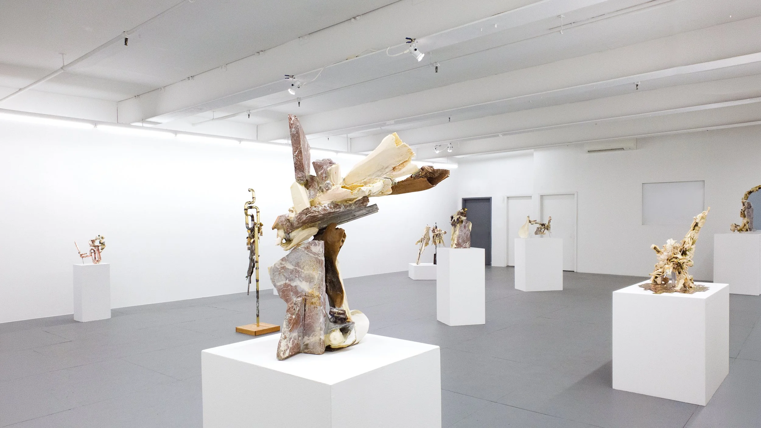 Yasue Maetake Transmutation gallery installation: non-representational sculpture of stacked granite and bone forms on a white pedestal in the center, other bone and metal sculptures arranged throughout the gallery space
