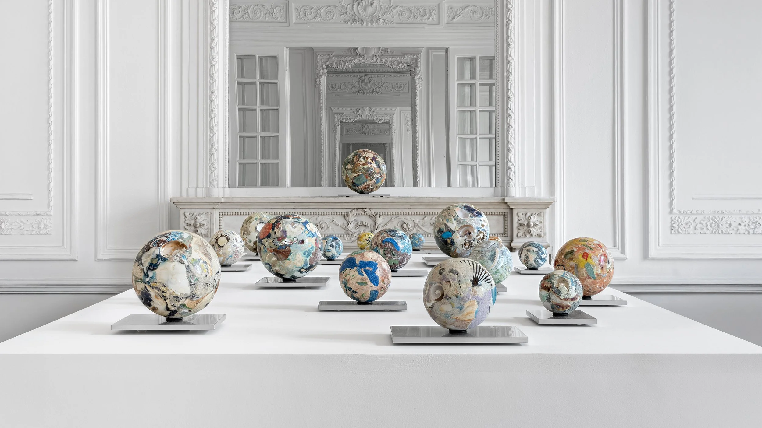 Yasue Maetake Orb Materia—Carved Algos gallery installation: deep perspective view of multicolored carved spheres arranged along a white platform, framed by European classical architecture and infinite mirror reflections