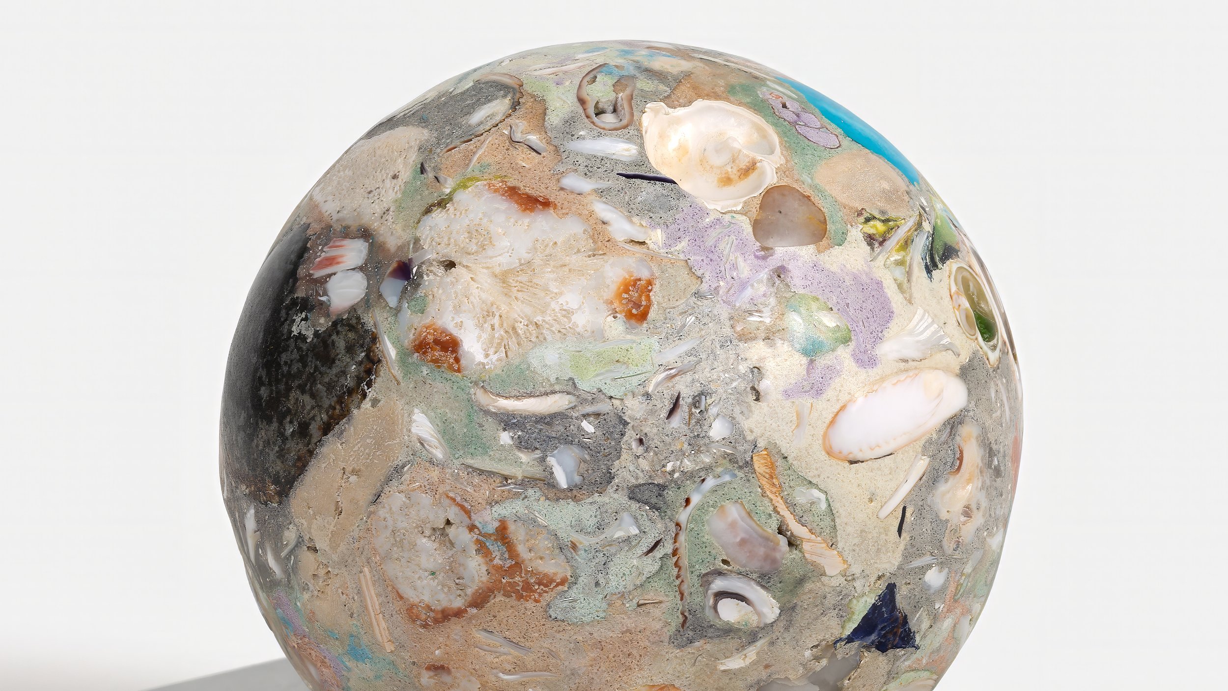 Yasue Maetake Orb Materia—Carved Algos detail: close-up of a carved sphere surface densely embedded with shells, coral-like textures, and multicolored mineral fragments