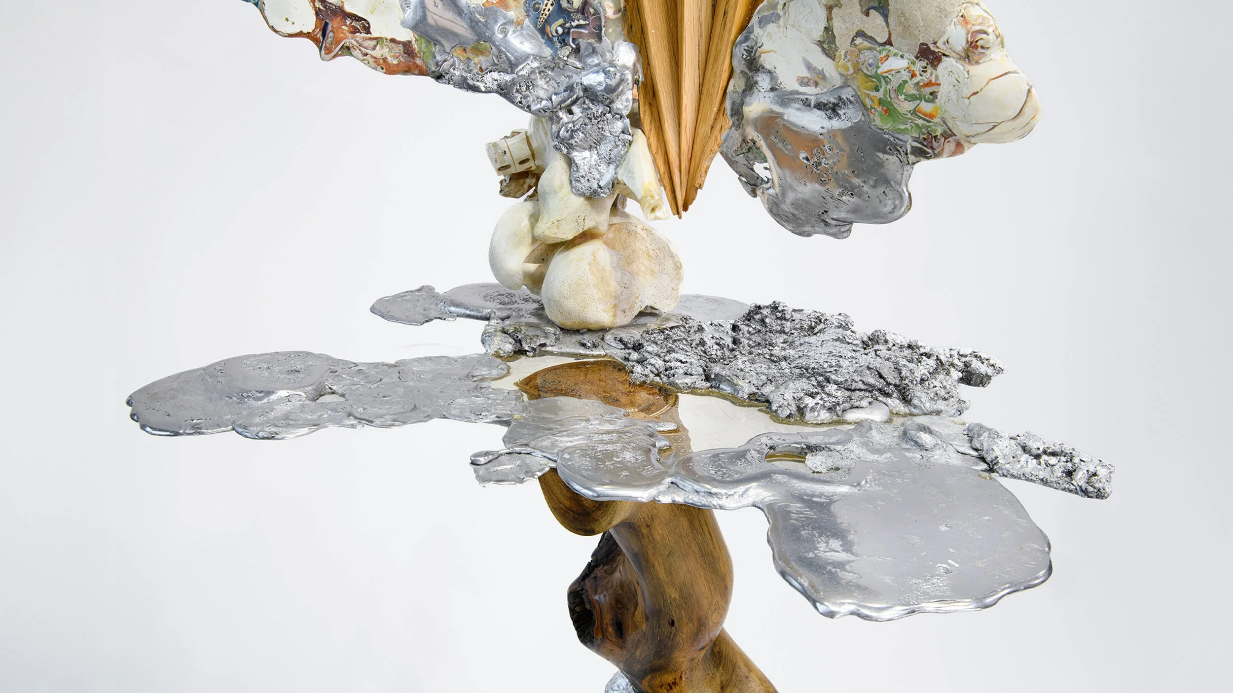Yasue Maetake Mare Fecunditatis detail: hybrid form with wooden base, reflective silver metallic surface, bone-like and colorful accretions, and wooden fan element against white background