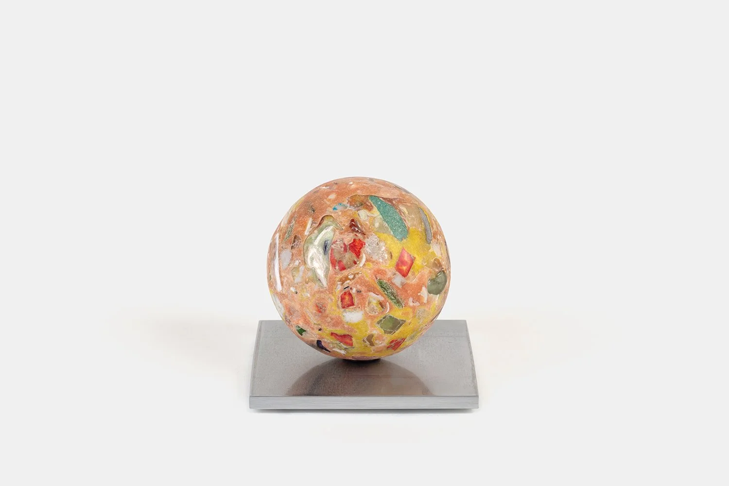 Yasue Maetake Orb Materia—Kohakutou, 2026. Warm orange and yellow spherical form with embedded red, green, and white mineral fragments, resting on a square aluminum base.