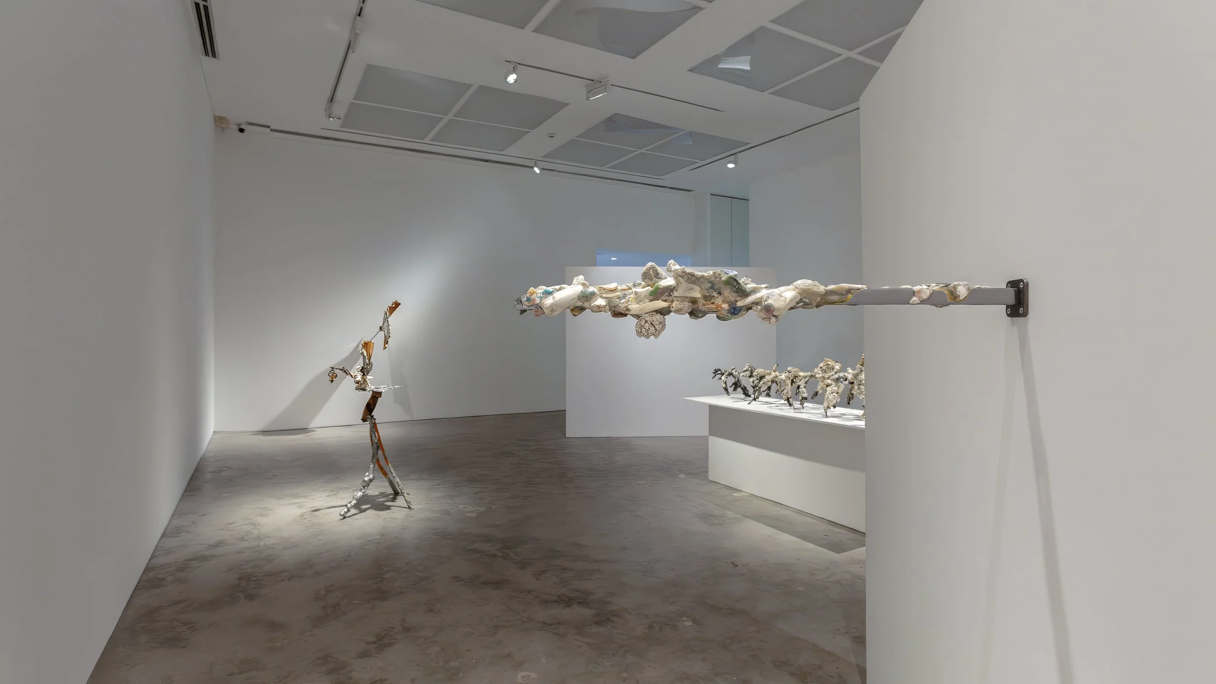 Yasue Maetake Mare Fecunditatis gallery installation: wide view with tall thin standing sculpture left, long horizontal wall-mounted organic form center, and row of small sculptures on white pedestal right in white gallery space