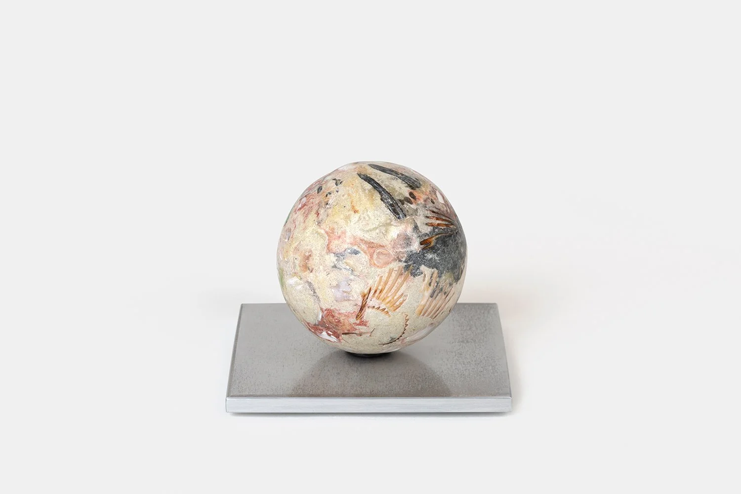 Yasue Maetake Orb Materia—Bird Tracks, 2026. Spherical form with soft beige mineral surface containing dark linear marks and fossil-like impressions, resting on a square aluminum base.