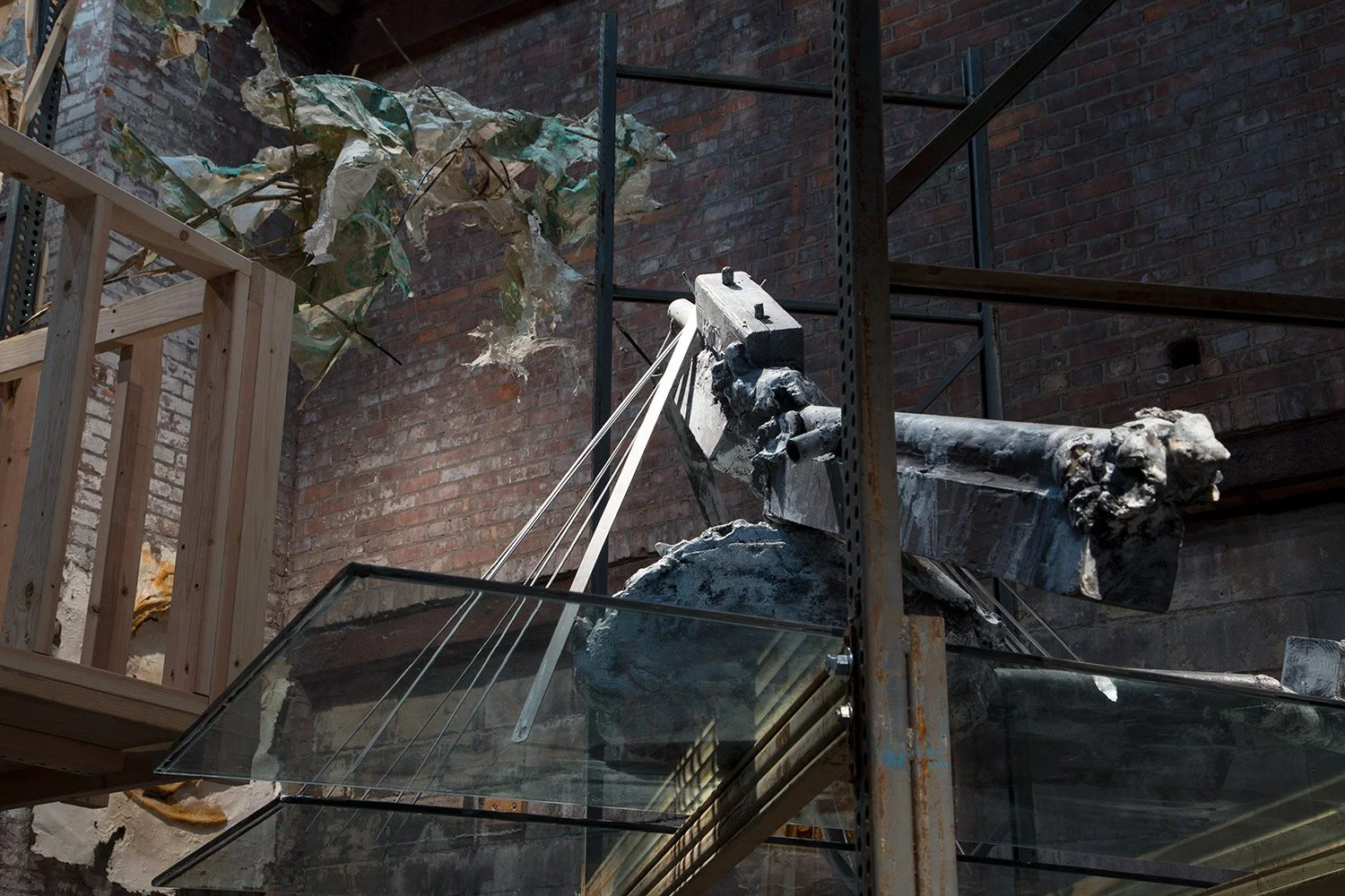 An art installation involving a large, weathered sculpted cannon and broken, colorful paper leaves on a metal structure against a brick wall.