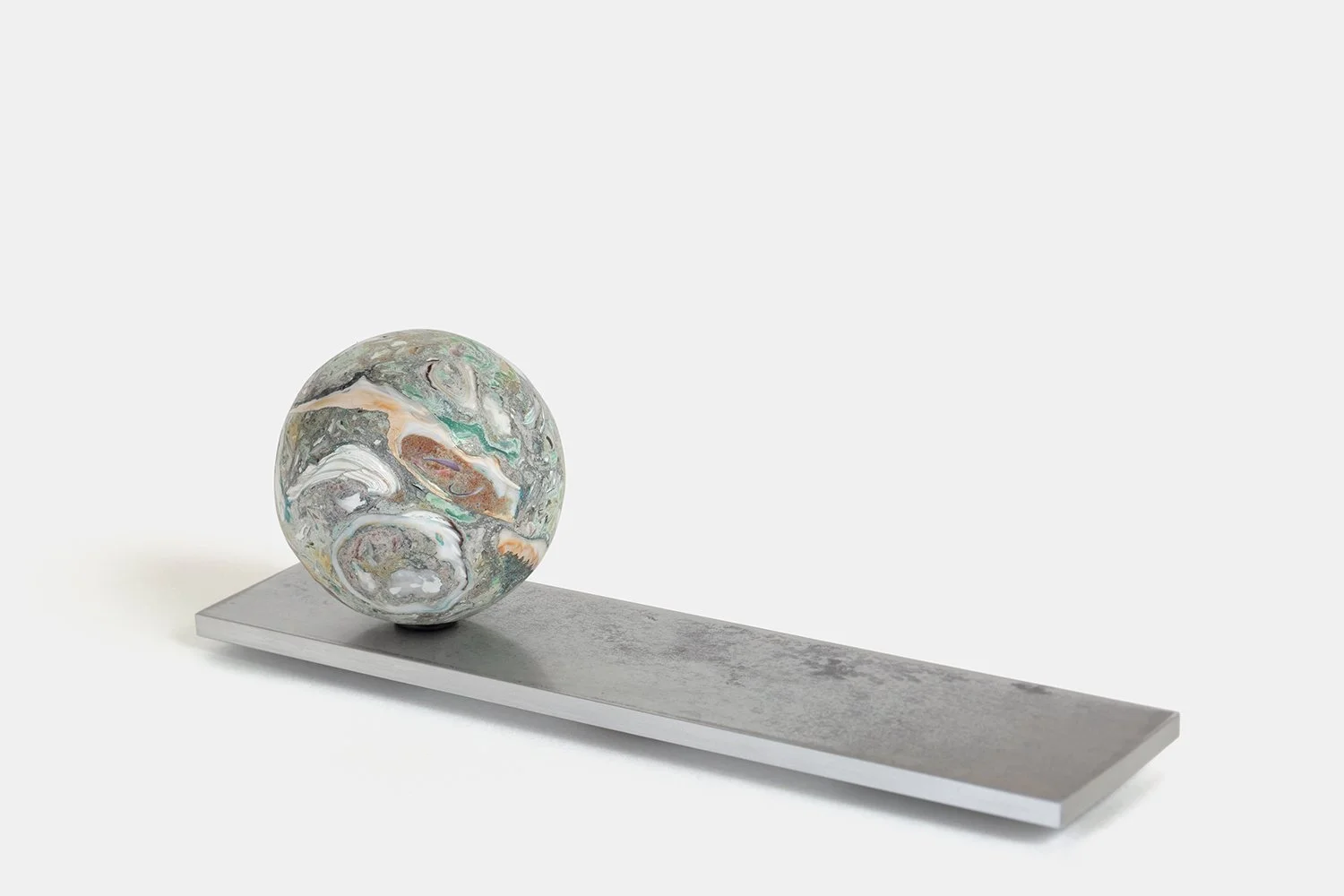 Yasue Maetake Orb Materia—Chlorophyll, 2026. Spherical form with soft green, white, and beige mineral surfaces containing shell fragments, positioned on the left side of a long rectangular aluminum base.