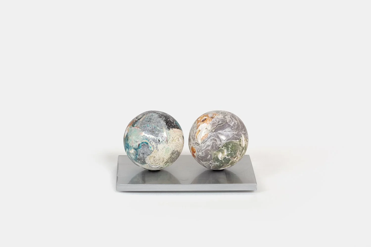 Yasue Maetake Orb Materia—Algae, 2026. Two spherical sculptures on a rectangular aluminum base, the left with cool blue-gray tones and the right with warmer gray, orange, and green mineral surfaces.