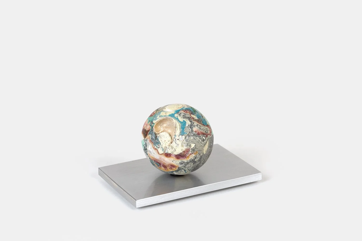 Yasue Maetake Orb Materia—Air Current, 2026. Spherical form with layered turquoise, reddish-pink, and gray mineral surfaces containing shell fragments, resting on a square aluminum base.