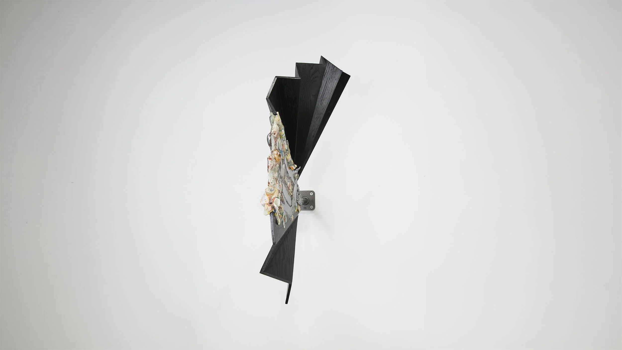 Yasue Maetake Mare Fecunditatis detail: frontal view of black pleated wooden fan wall piece with protruding multicolored organic form of shells, stones, and metallic elements against white background