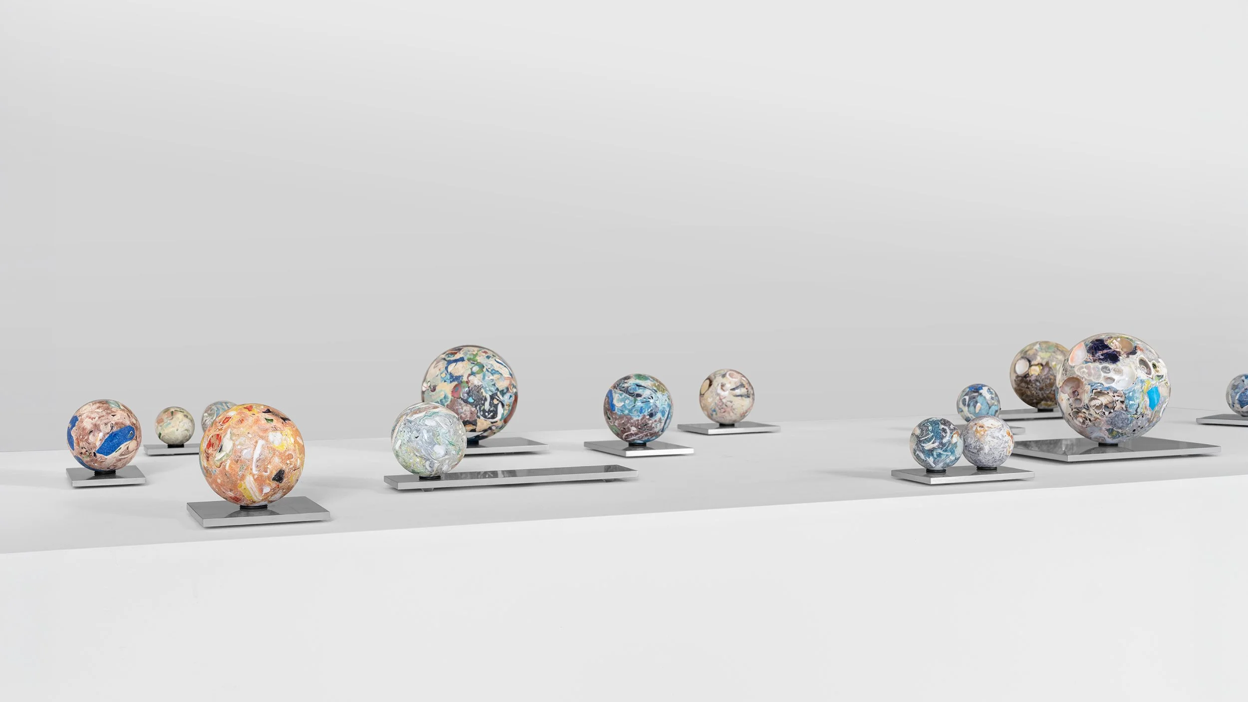 Yasue Maetake Orb Materia—Carved Algos: long horizontal arrangement of multicolored carved spheres of varying sizes on aluminum bases against a plain light background