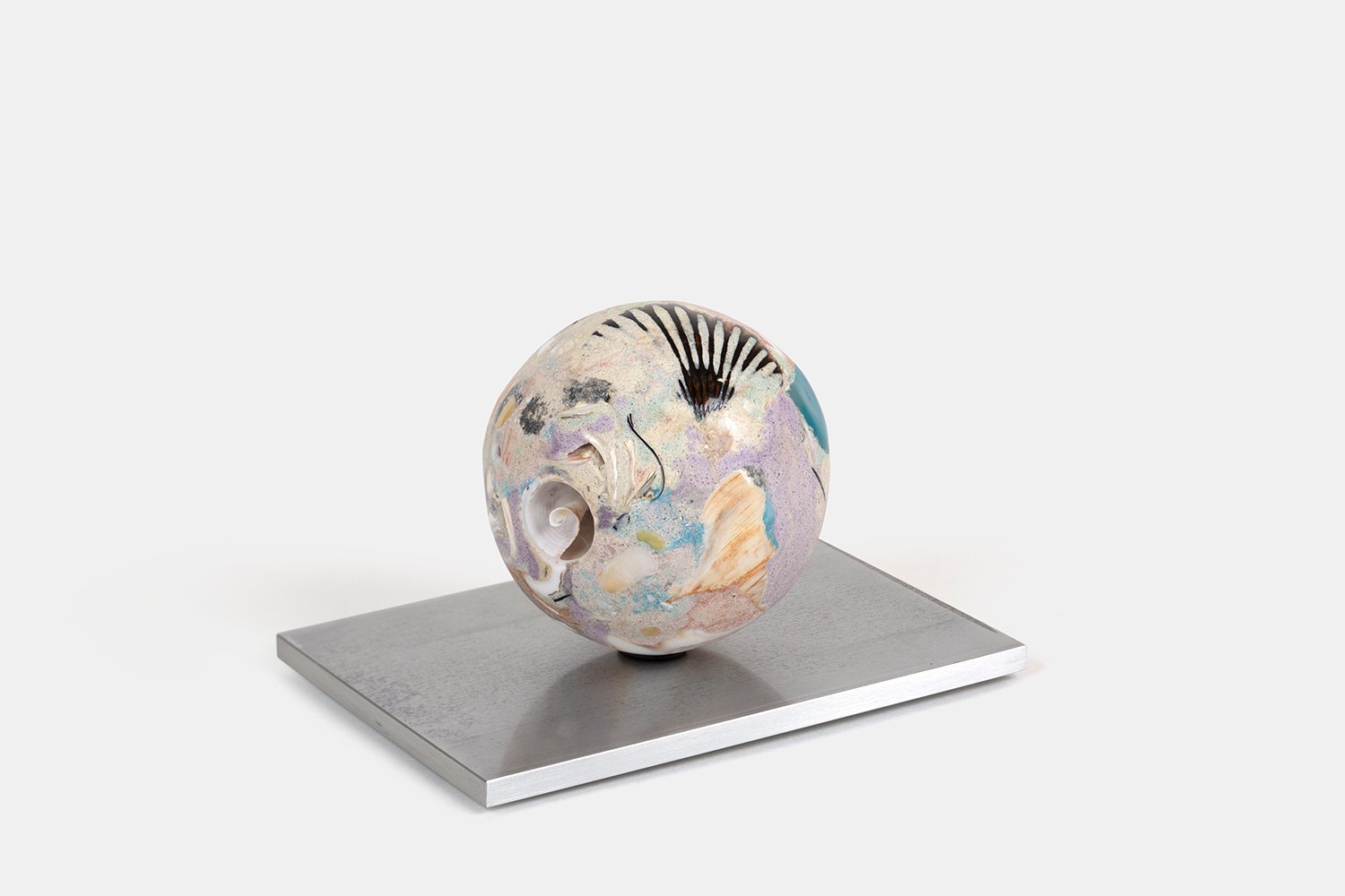 Yasue Maetake Orb Materia—Cyclone-glyph, 2026. Spherical form with soft lavender and cream surface, a black fan-like mark, and embedded shell fragments on a square aluminum base.