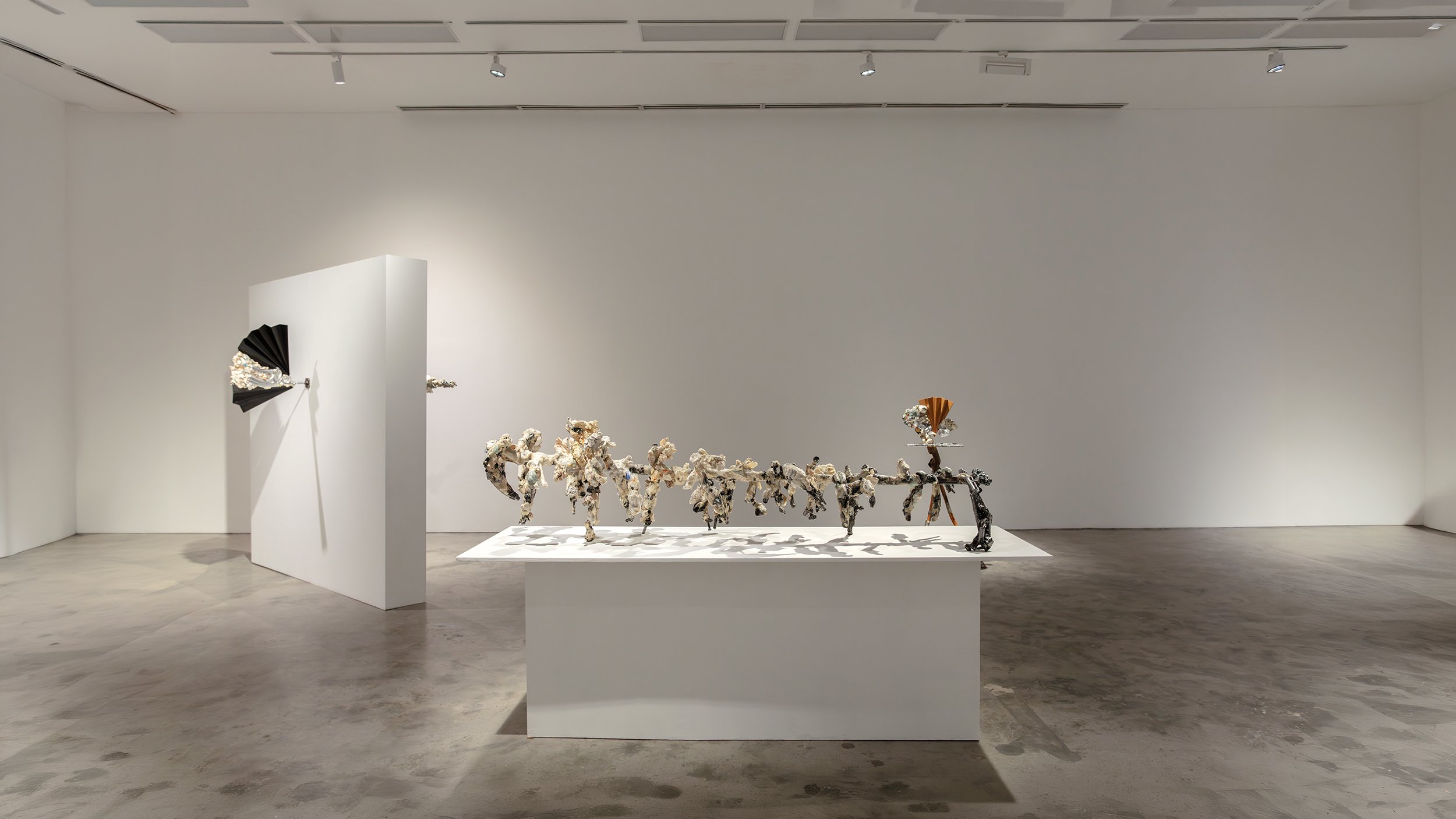 Yasue Maetake Mare Fecunditatis gallery view: black fan-shaped piece wall-mounted left, long pedestal with row of multicolored dangling growth-like forms right in white space