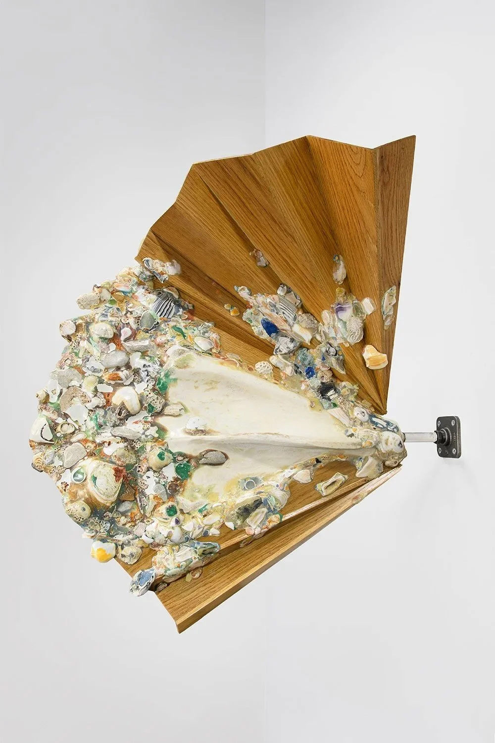 Yasue Maetake, Ceremonial Delta II, 2025. Wall-mounted hybrid sculpture featuring a large light-brown pleated oak fan structure with a dense, protruding organic form composed of multicolored shells, stones, and textured materials.