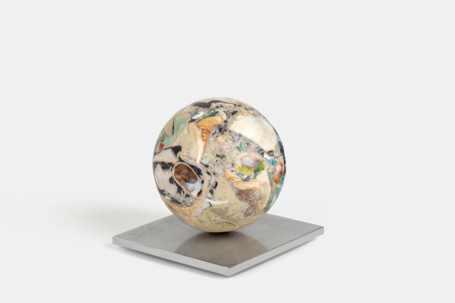 Yasue Maetake Orb Materia—Silken, 2026. Spherical form with soft beige mineral surface, deep hollow cavity, and mixed black and white shell fragments, resting on a square aluminum base.