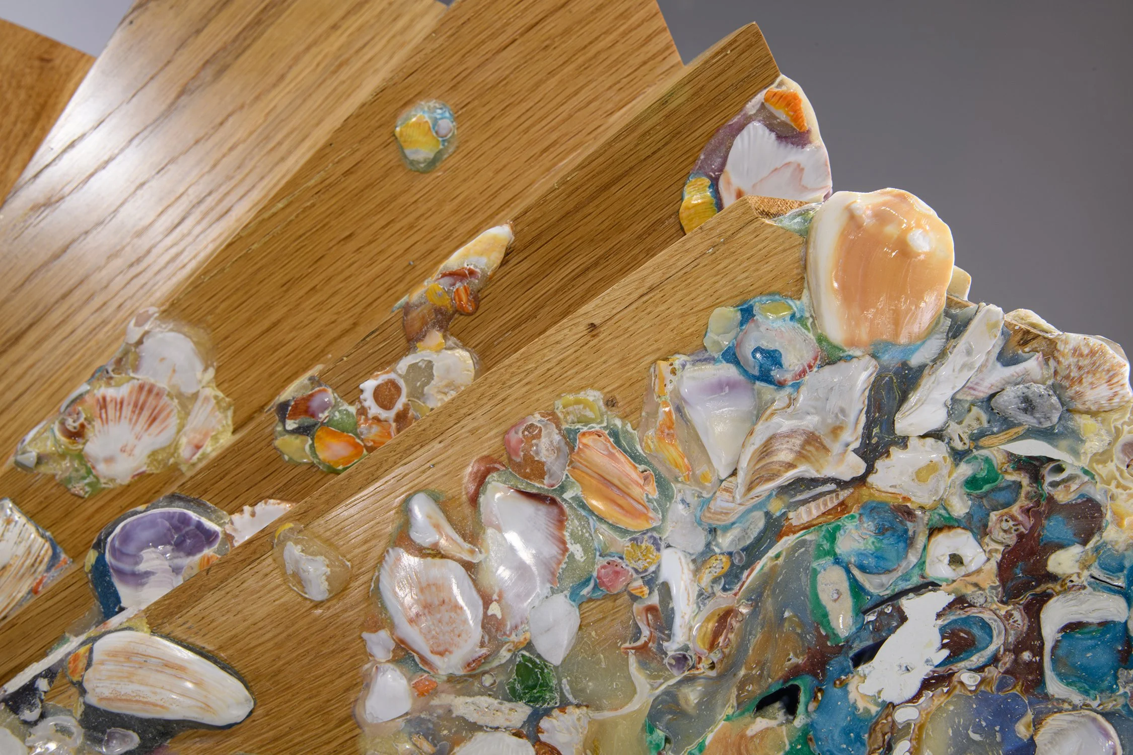 Yasue Maetake Mare Fecunditatis close-up: polished natural color wooden surface with multicolored shells, stones, and textured materials attached against gray background