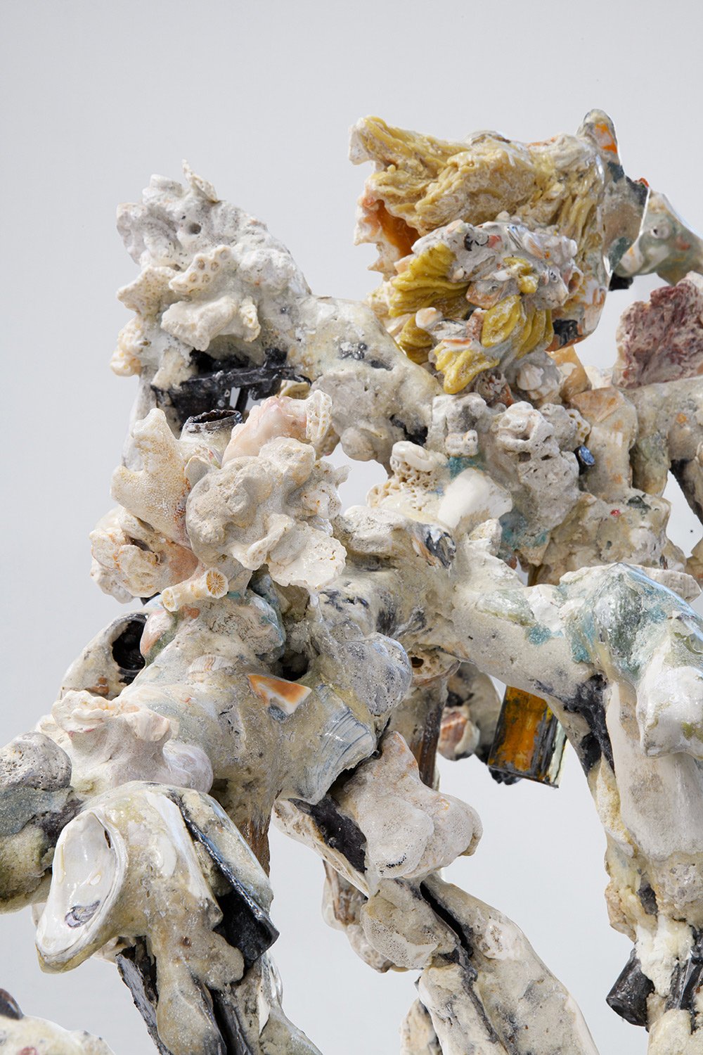 Yasue Maetake's sculpture Mare Fecunditatis – resurrection, 2025. Close-up detail of the dense, coral-like cluster of the hybrid sculpture showing rough, porous white and gray forms with multicolored glaze accents, embedded shells, and dark metallic 