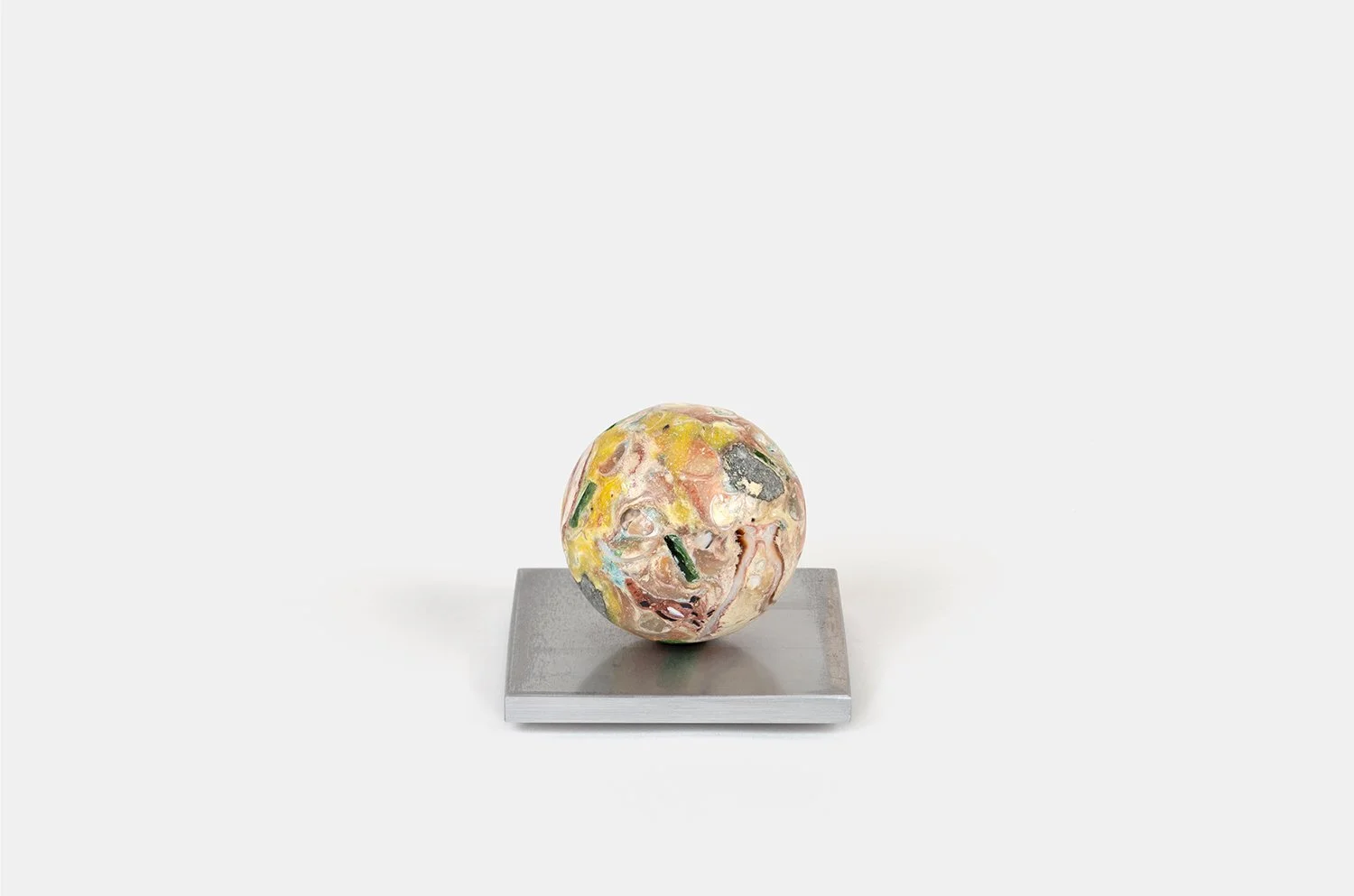 Yasue Maetake Orb Materia—Yuzu, 2026. Compact spherical form with mottled yellow and pink surface containing bright and dark mineral fragments, resting on a square aluminum base.