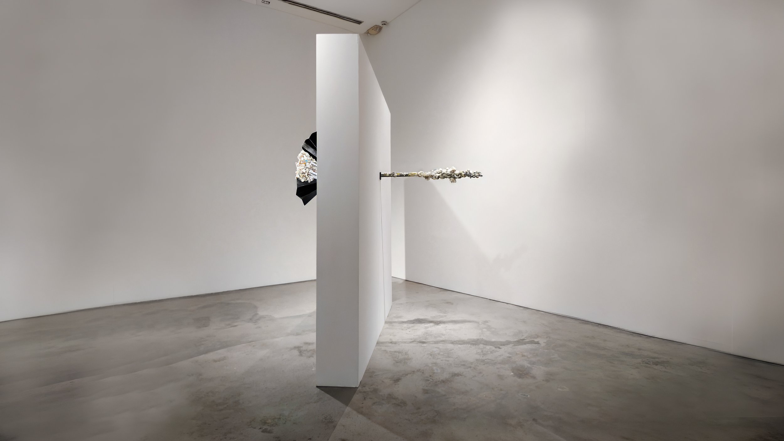 Yasue Maetake Mare Fecunditatis gallery view: black fan-shaped piece wall-mounted on panel left, short metallic bar with small dangling forms wall-mounted right in white space