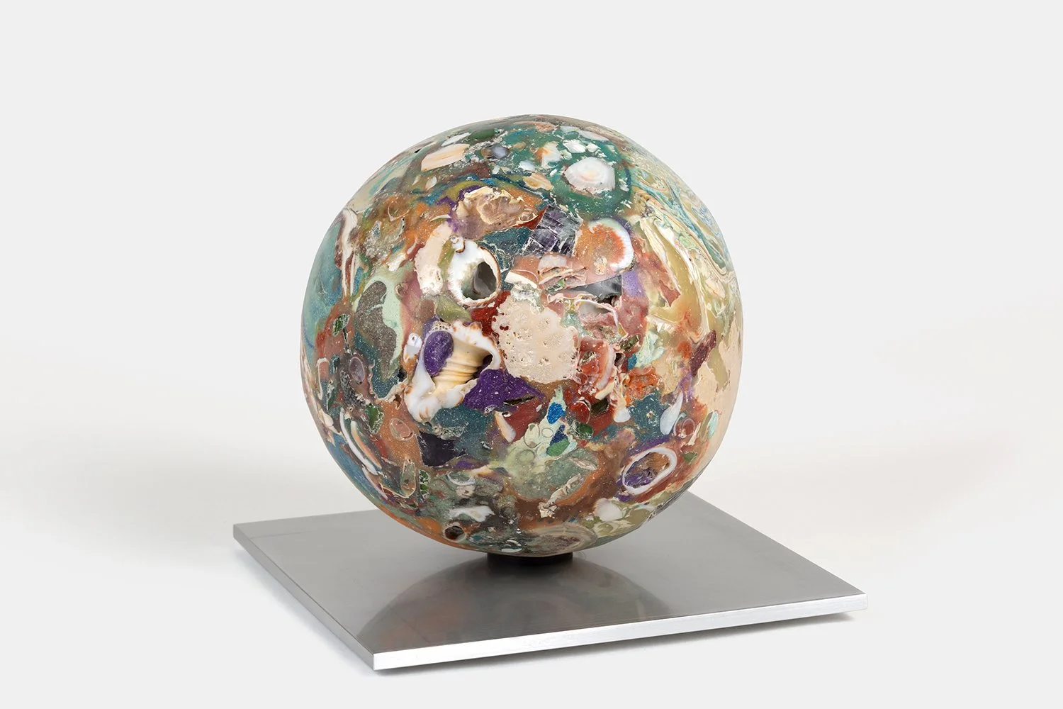 Yasue Maetake Orb Materia—Inlet Swallowtail, 2026. Large spherical form with dense purple, red-brown, green, and beige mineral surfaces containing open shell cavities, resting on a square aluminum base.