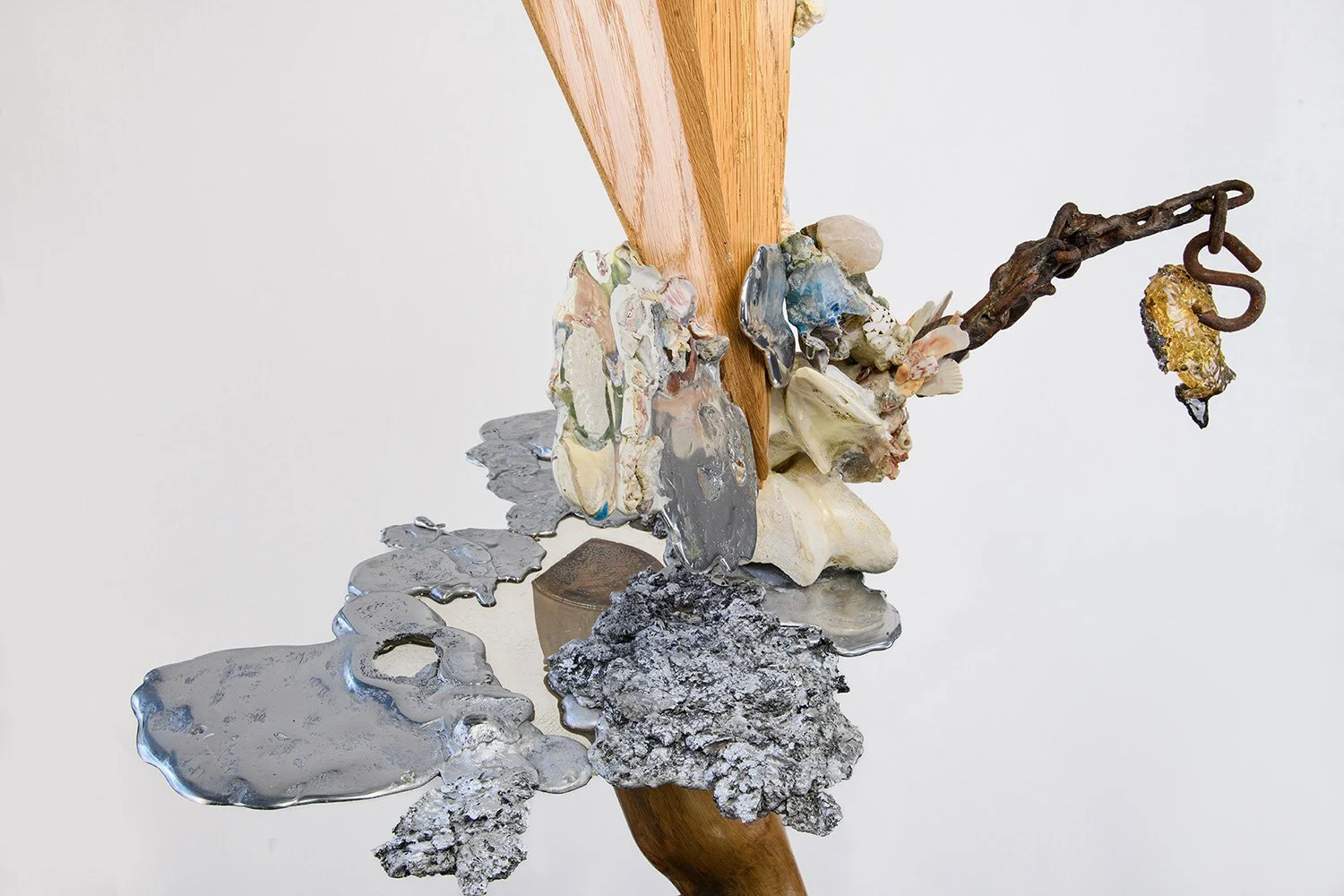 Yasue Maetake's abstract sculpture made of wood, metal, shells, and various textured materials, with a rusty chain hanging from the right side.