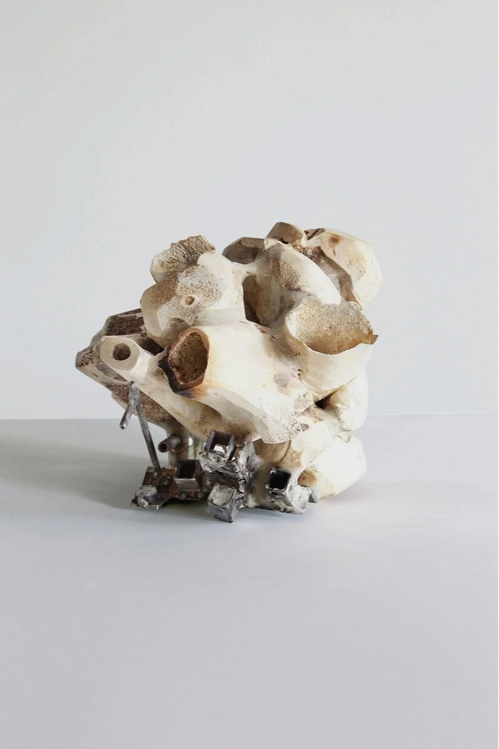 Yasue Maetake’s sculpture Symbolic Atmosphere III, 2019. Compact hybrid form of layered animal bones combined with steel elements, resting on a light gray surface.