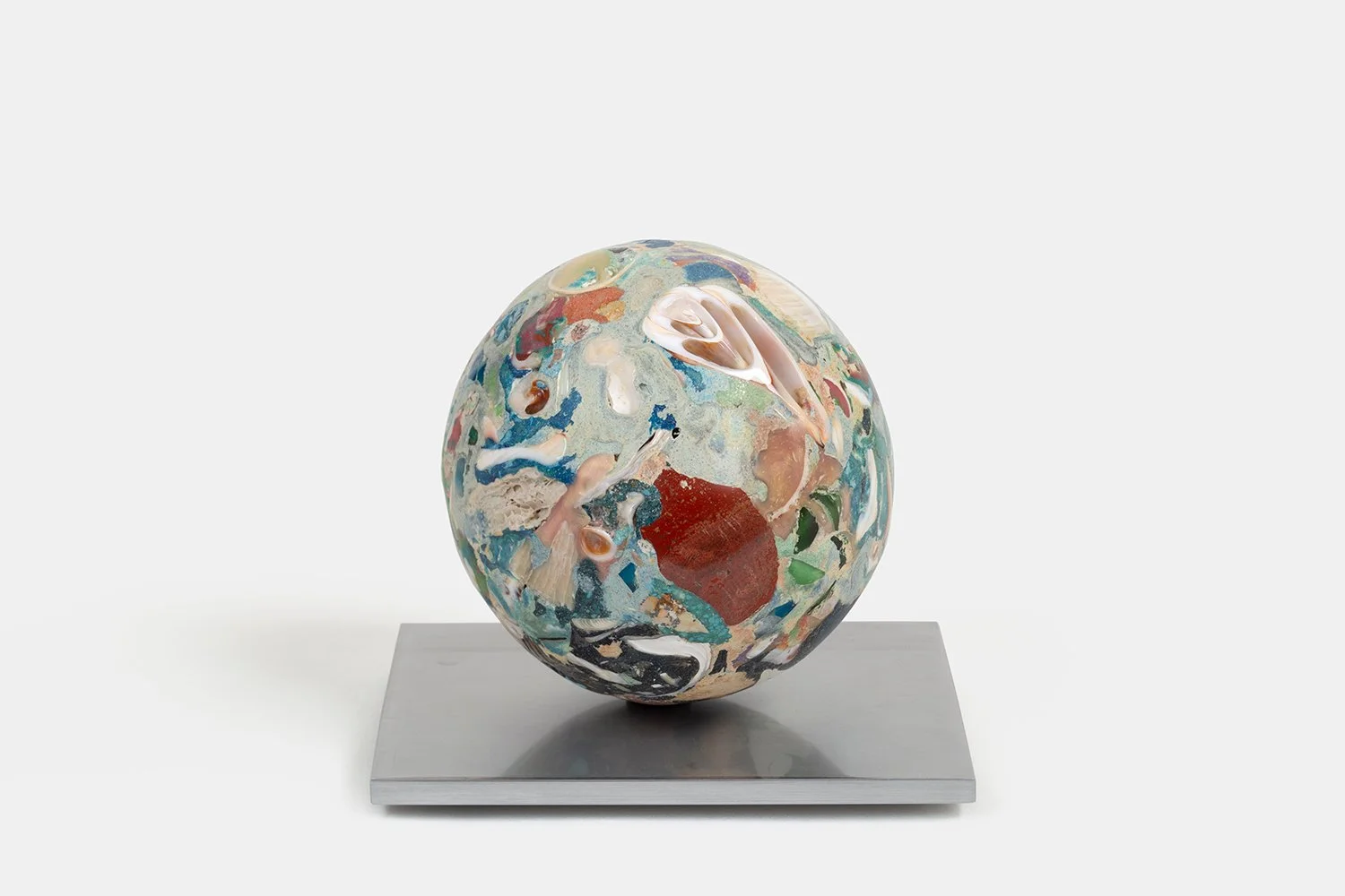 Yasue Maetake Orb Materia—Chigiri-e, 2026. Colorful spherical sculpture with layered blue, red, green, and white mineral surfaces containing shell fragments, resting on a square aluminum base.