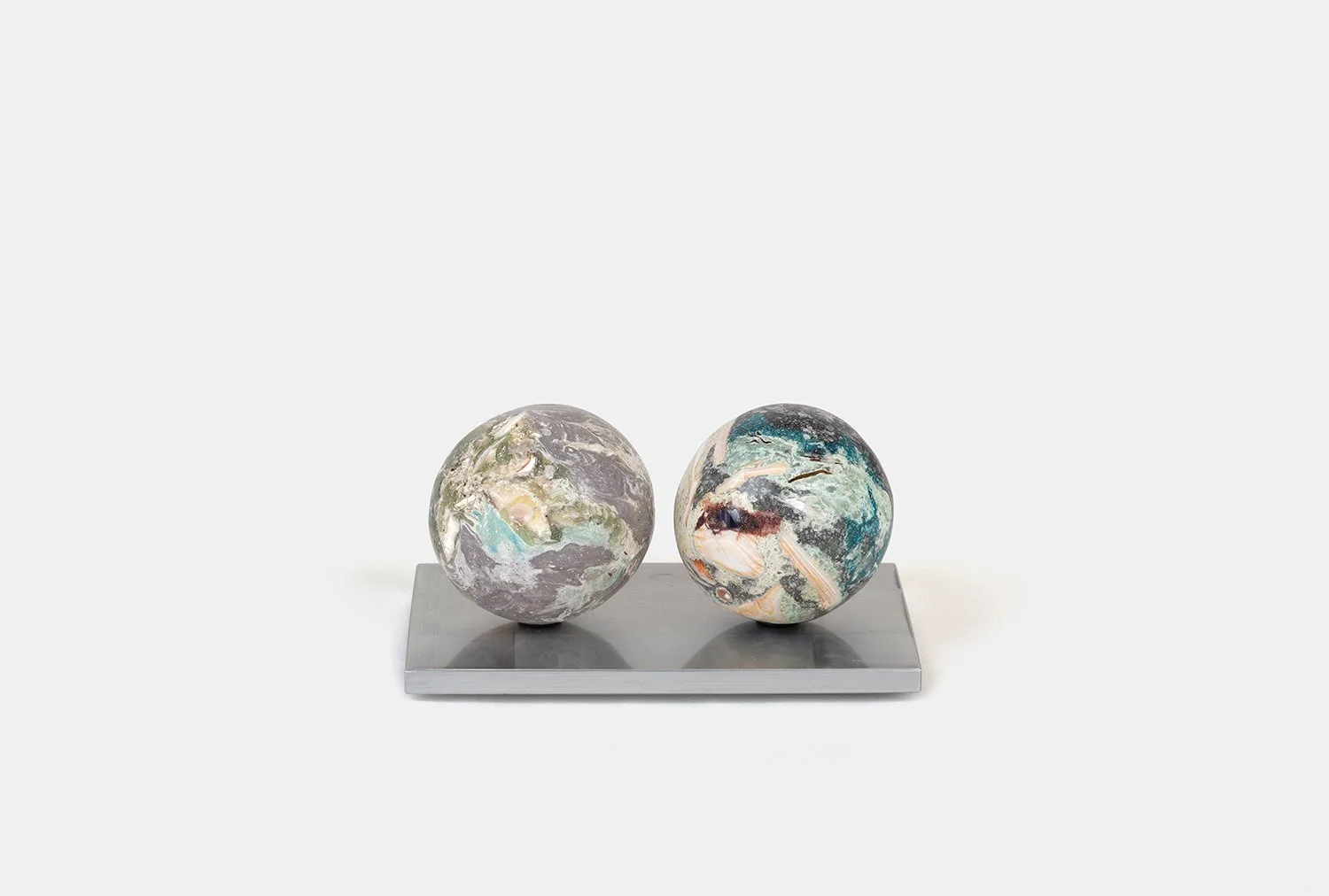 Yasue Maetake Orb Materia—Algae, 2026. Two spherical sculptures side by side on a shared rectangular aluminum base, with gray-green and teal mineral surfaces containing embedded shell fragments.