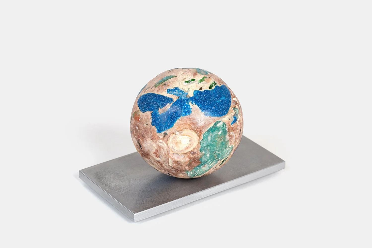 Yasue Maetake Orb Materia—Blue First Aid, 2026. Spherical form with large deep blue mineral areas across a warm beige surface containing green and shell fragments, resting on a square aluminum base.