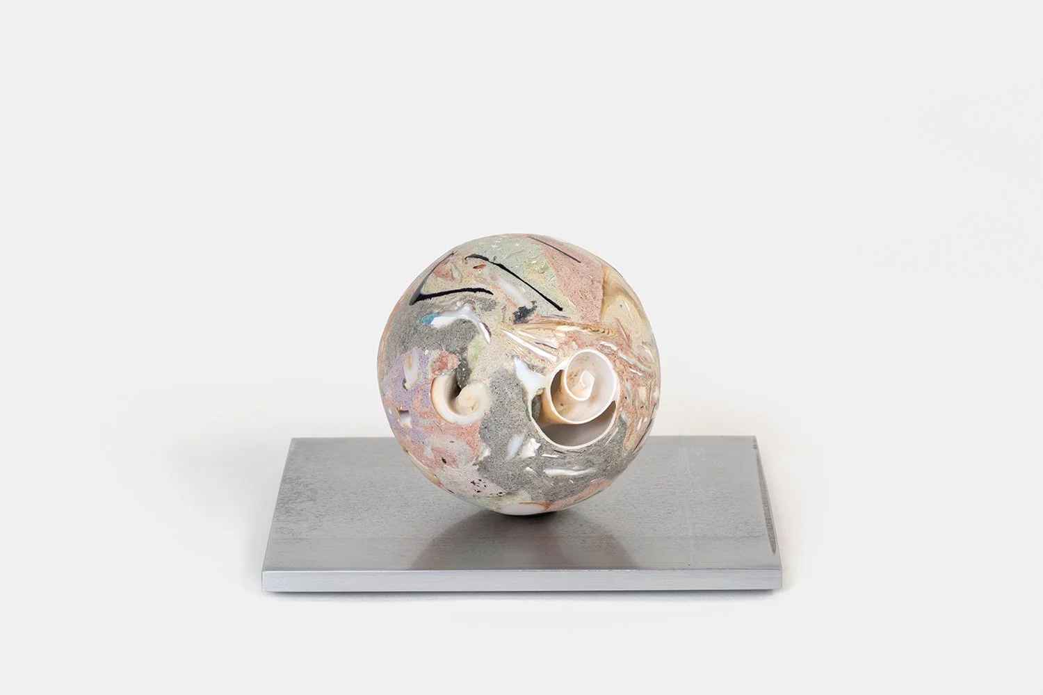 Yasue Maetake Orb Materia—Cyclone Glyph, 2026. Spherical form with soft pink, beige, and gray mineral surfaces containing open spiral shell cavities and thin black linear marks, resting on a square aluminum base.